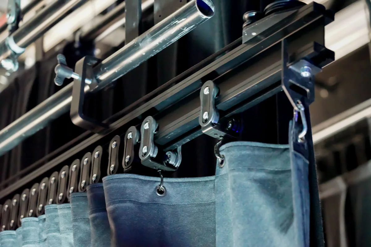 Track clamped to a pipe batten with roller carriers supporting a drape by its eyelets