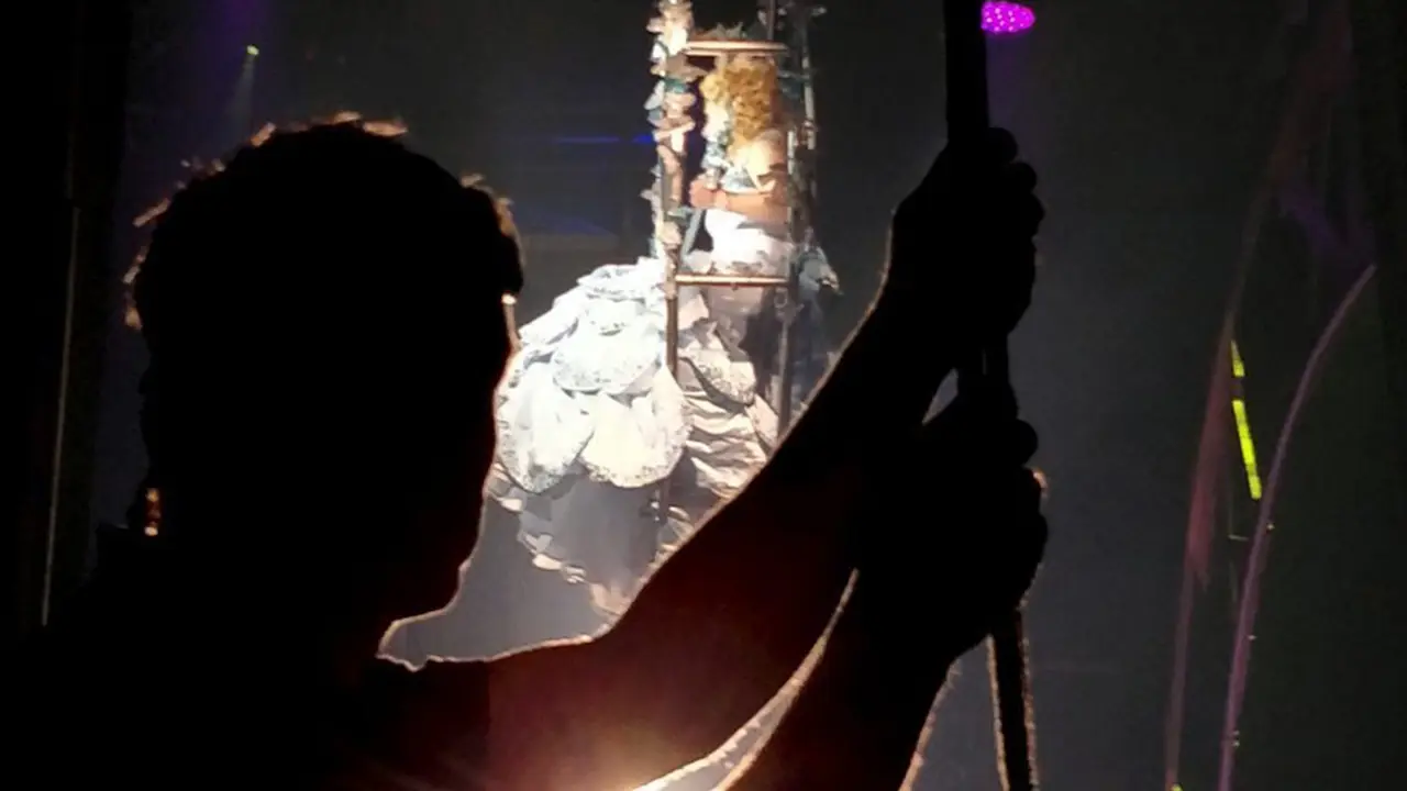 Backstage operator silhouette watches a costumed performer flown on rigging during a show