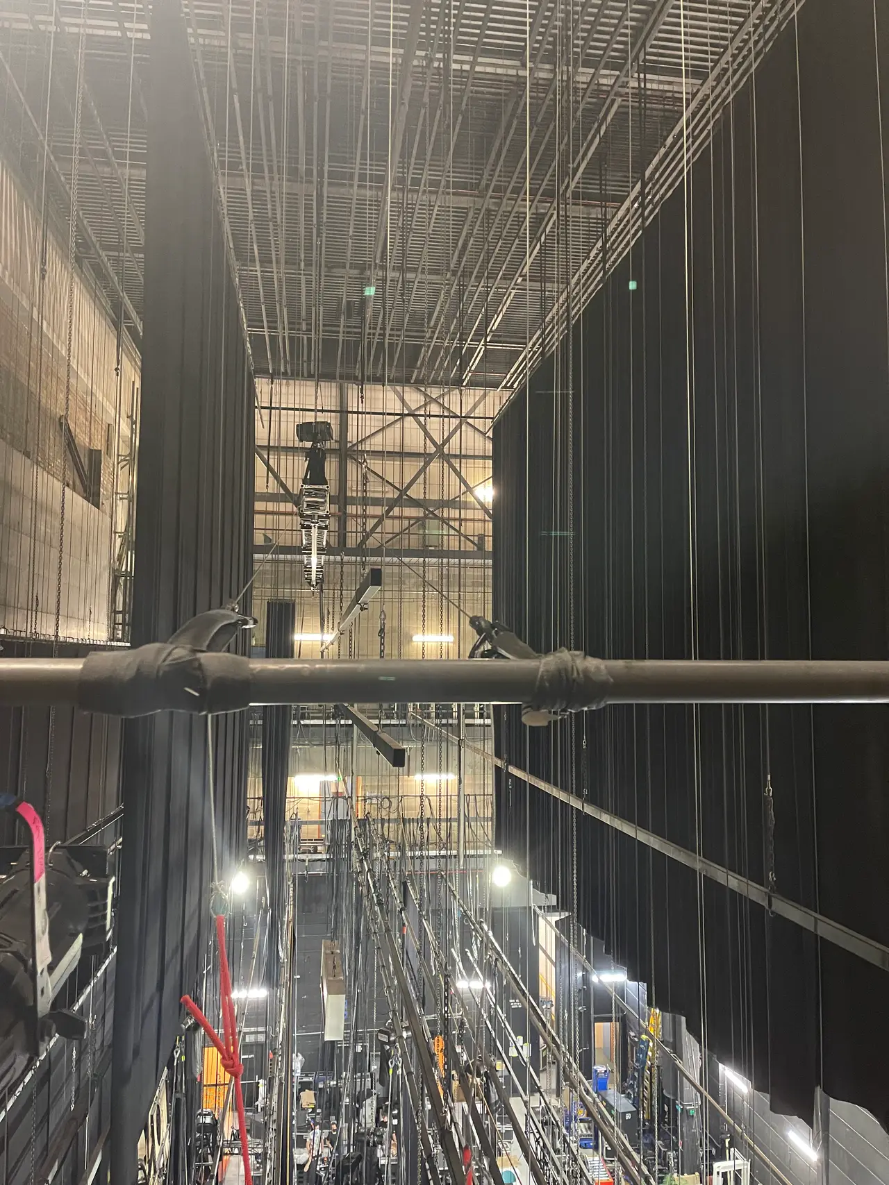 The fly tower grid with pipe battens and a hoist motor hanging among black legs.