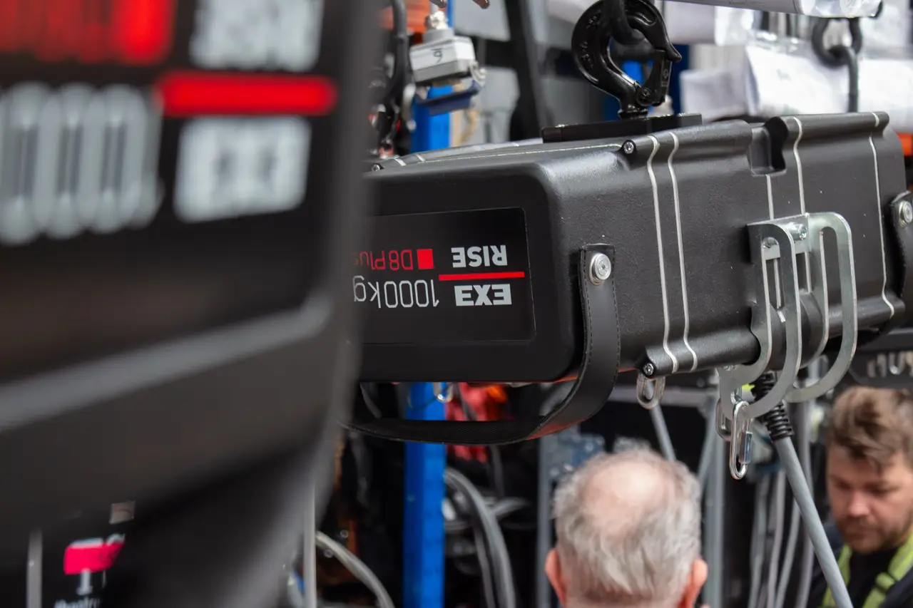 Close-up of an EXE Rise 1000kg chain hoist with digital display and hook, staff in background