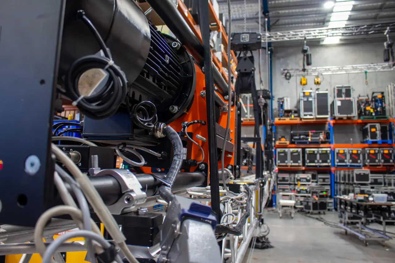 Close-up of a hoist motor and cabling with warehouse flight-case racking in the background