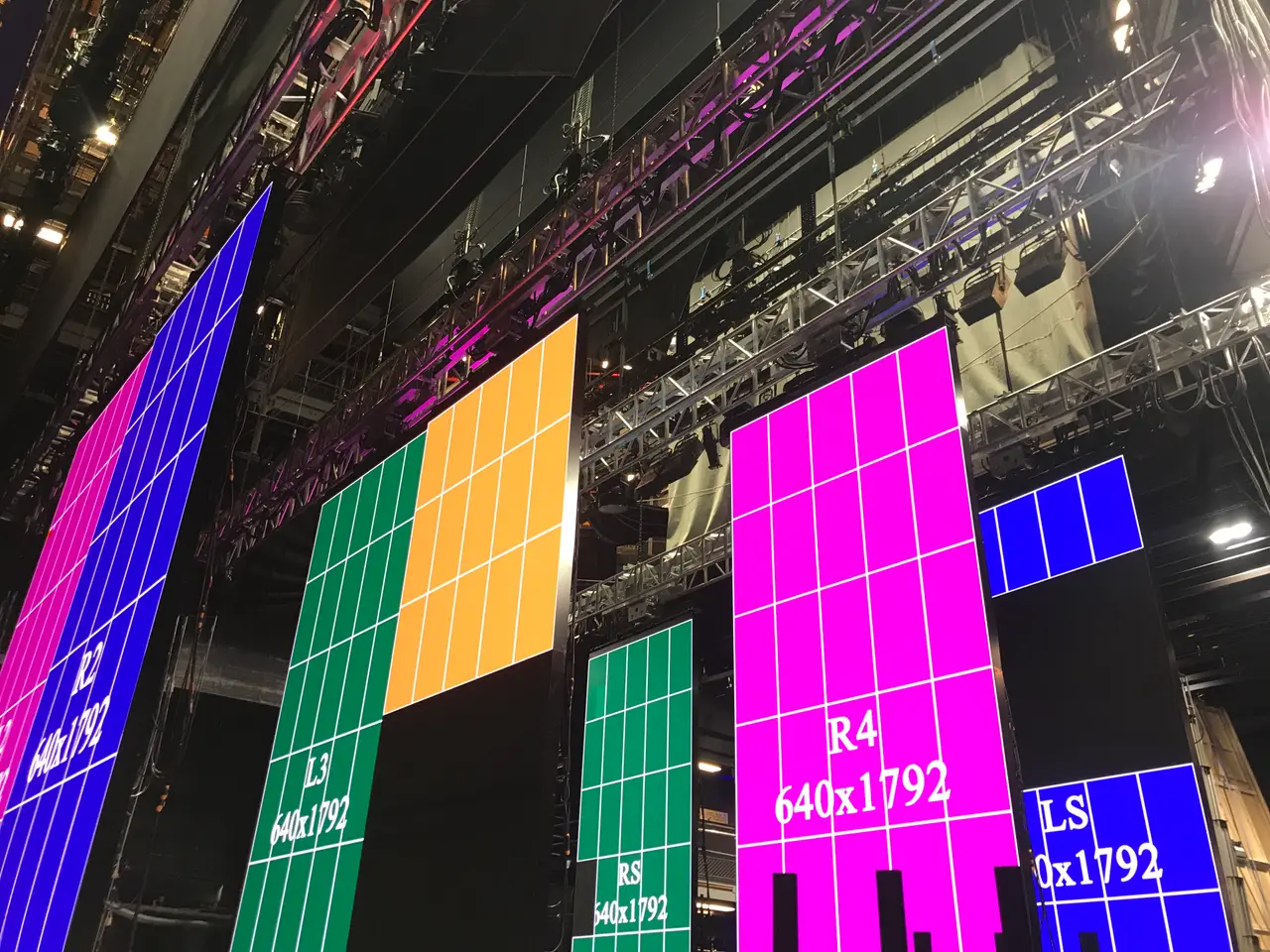 Coloured LED panels being mapping-tested in the fly tower with truss rigging above