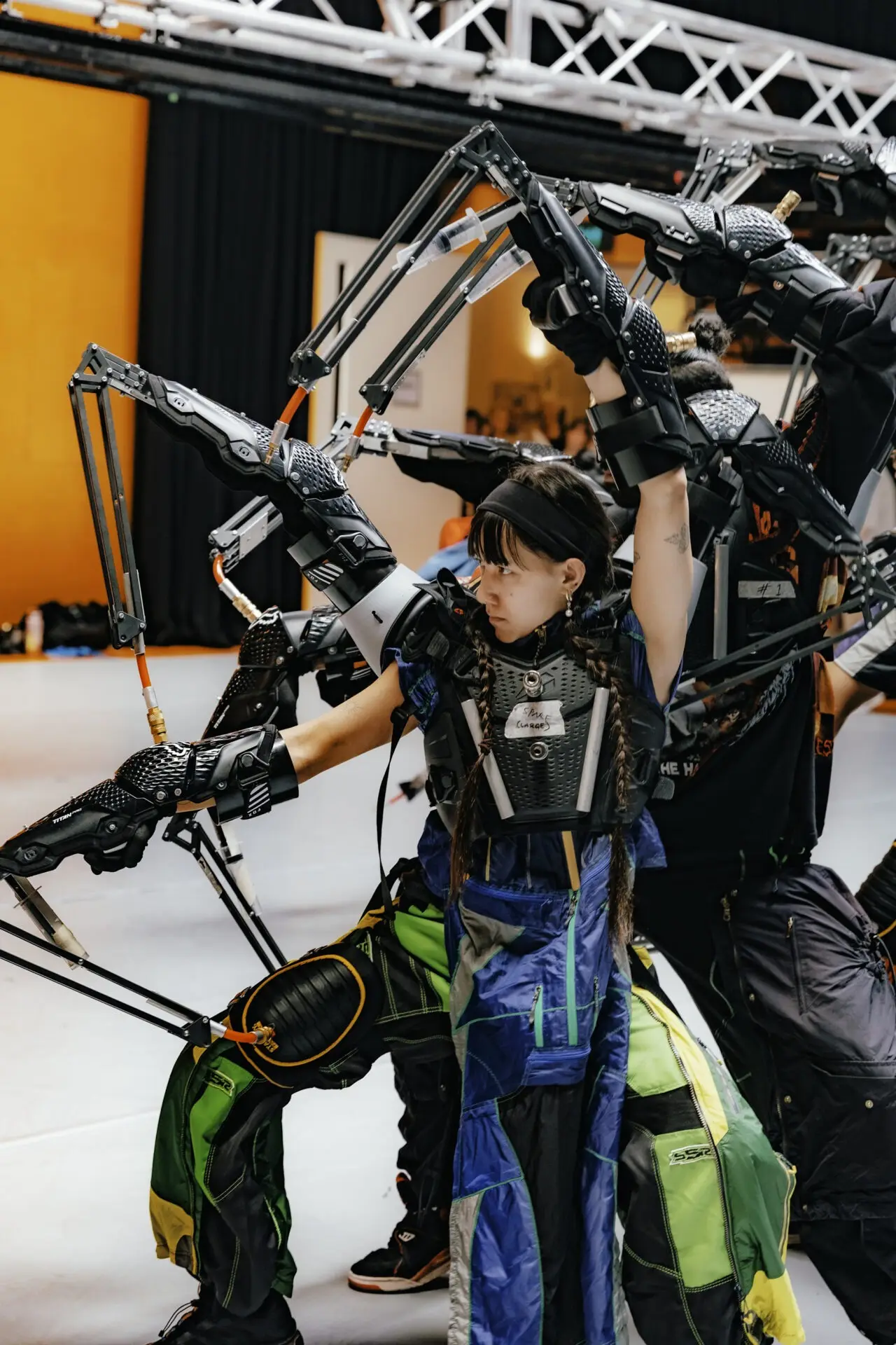 Dancer in robotic arm costume reaching up in rehearsal, truss above