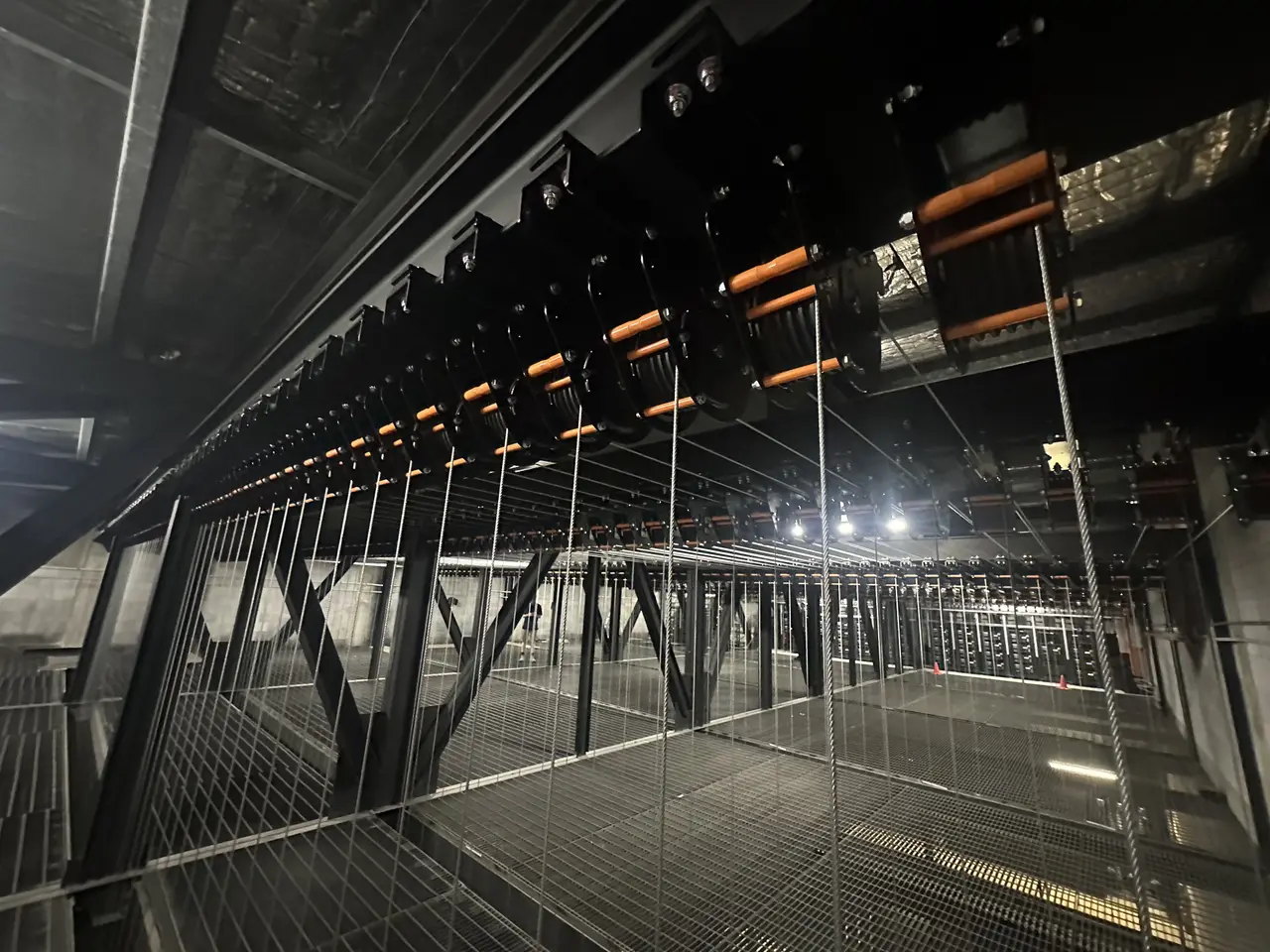 A long row of black loft block pulleys above a mesh catwalk in a fly tower grid.