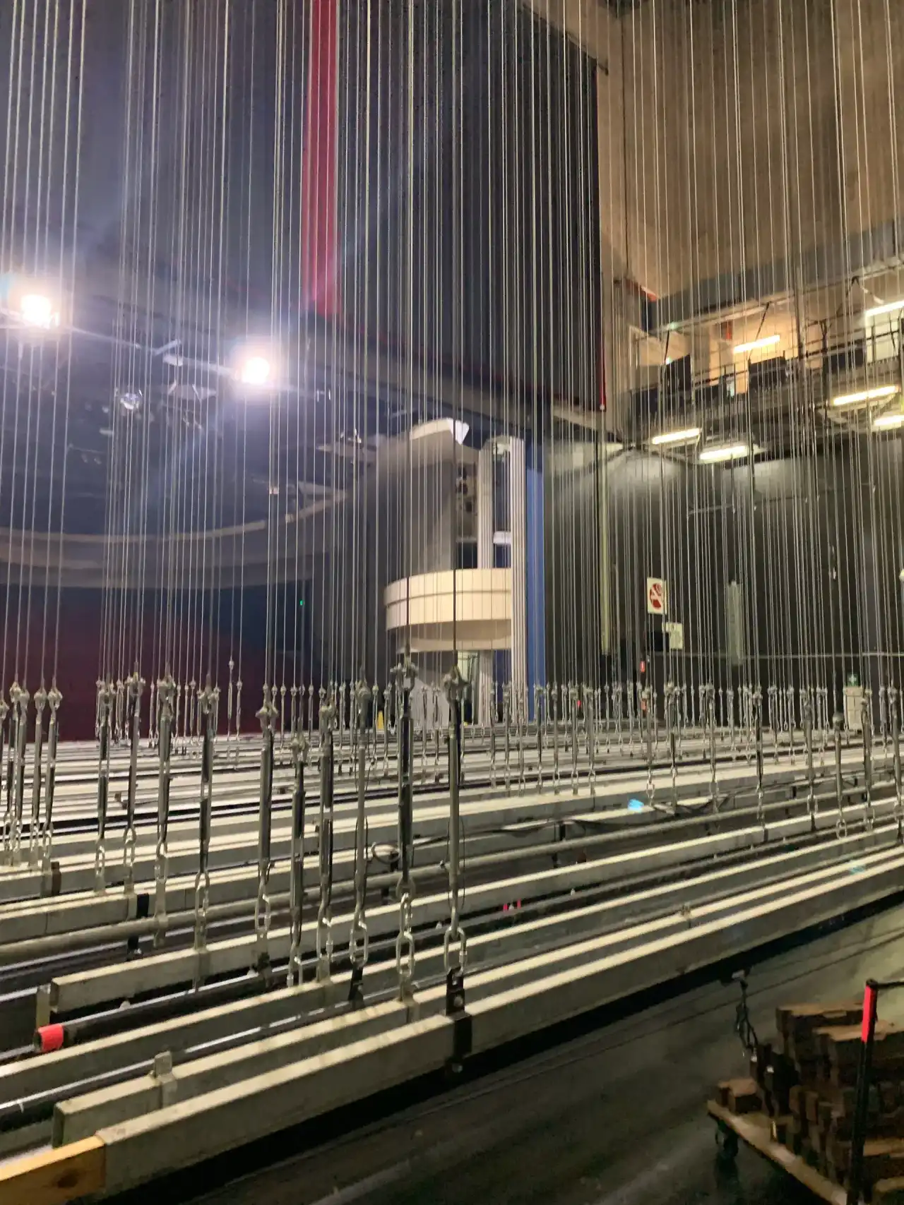 Rows of wire rope lines with turnbuckles running up through a theatre fly system.