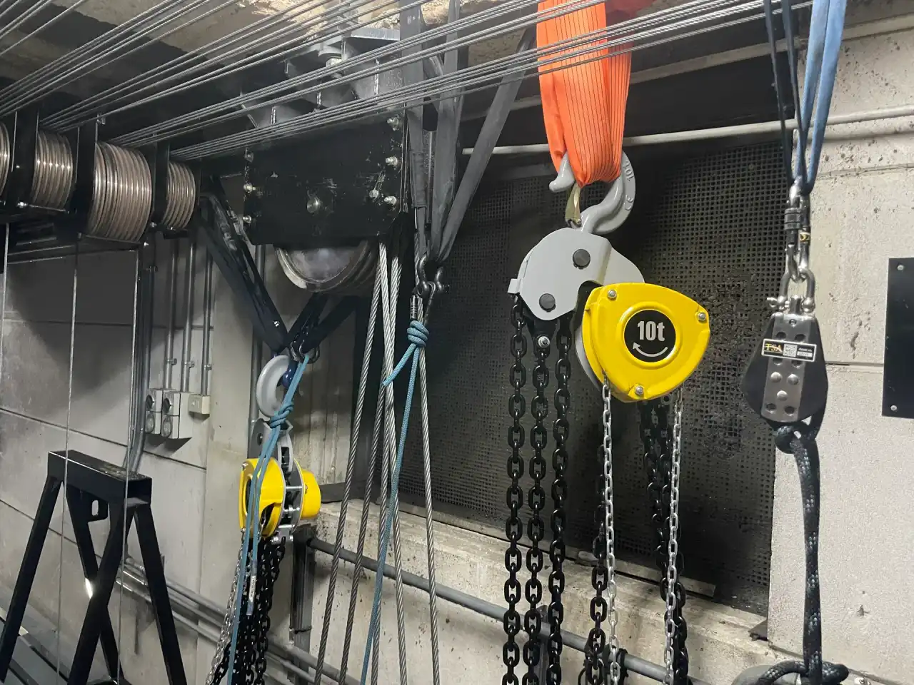 Yellow chain hoist, slings and shackles hanging in a theatre fly tower.