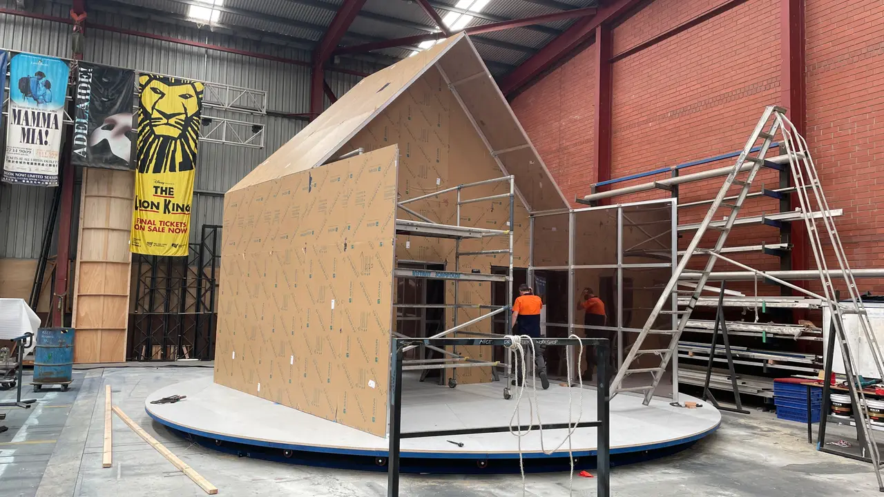 Peaked house-shaped set frame being built on a revolve in the scenic workshop