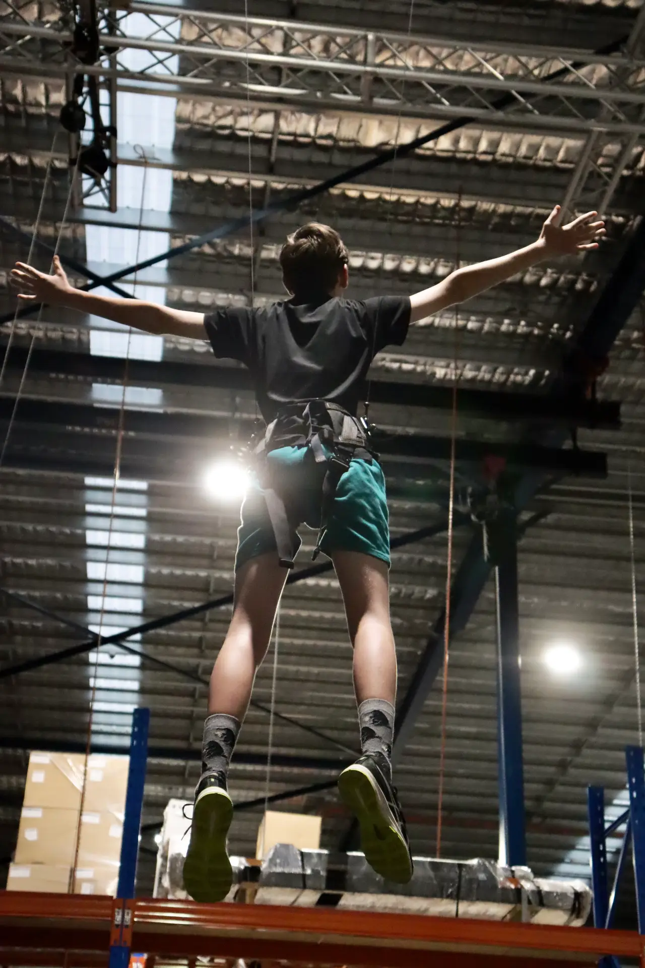 Rear view of a boy flown high near the warehouse roof, arms spread wide