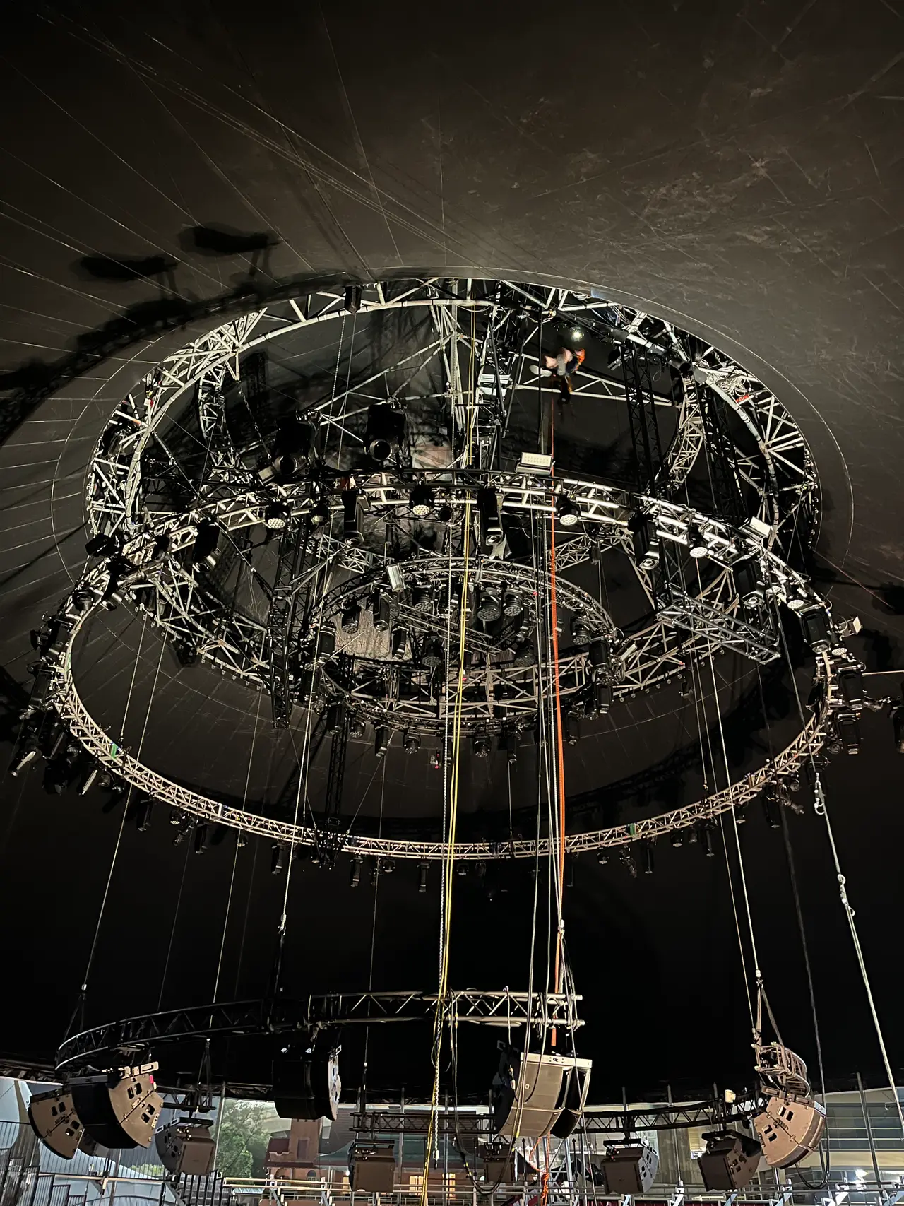 Rope access rigger descends through the truss lighting rig above lit seating at night