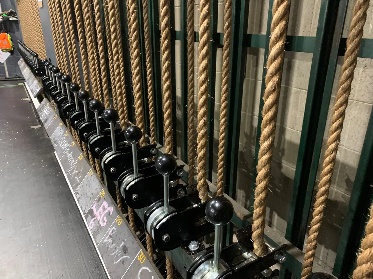 Black counterweight rope locks lined up on a locking rail, with manila operating lines running up beside them.