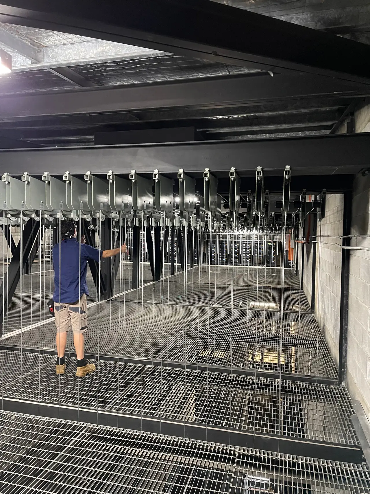 Technician beside a bank of suspended fly bars and wire lines under a steel grid