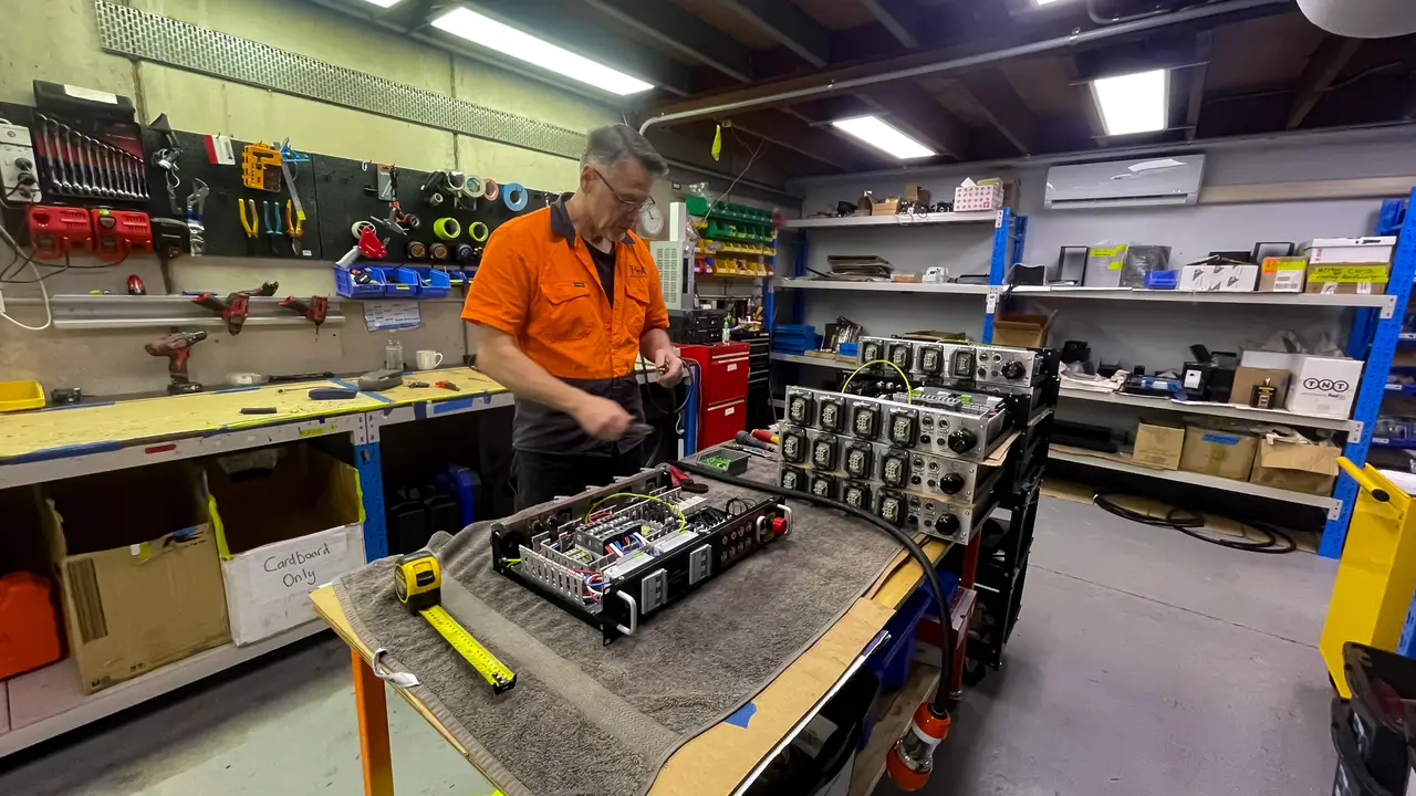 A TSA technician services a stacked chain hoist control rack on the workshop bench.