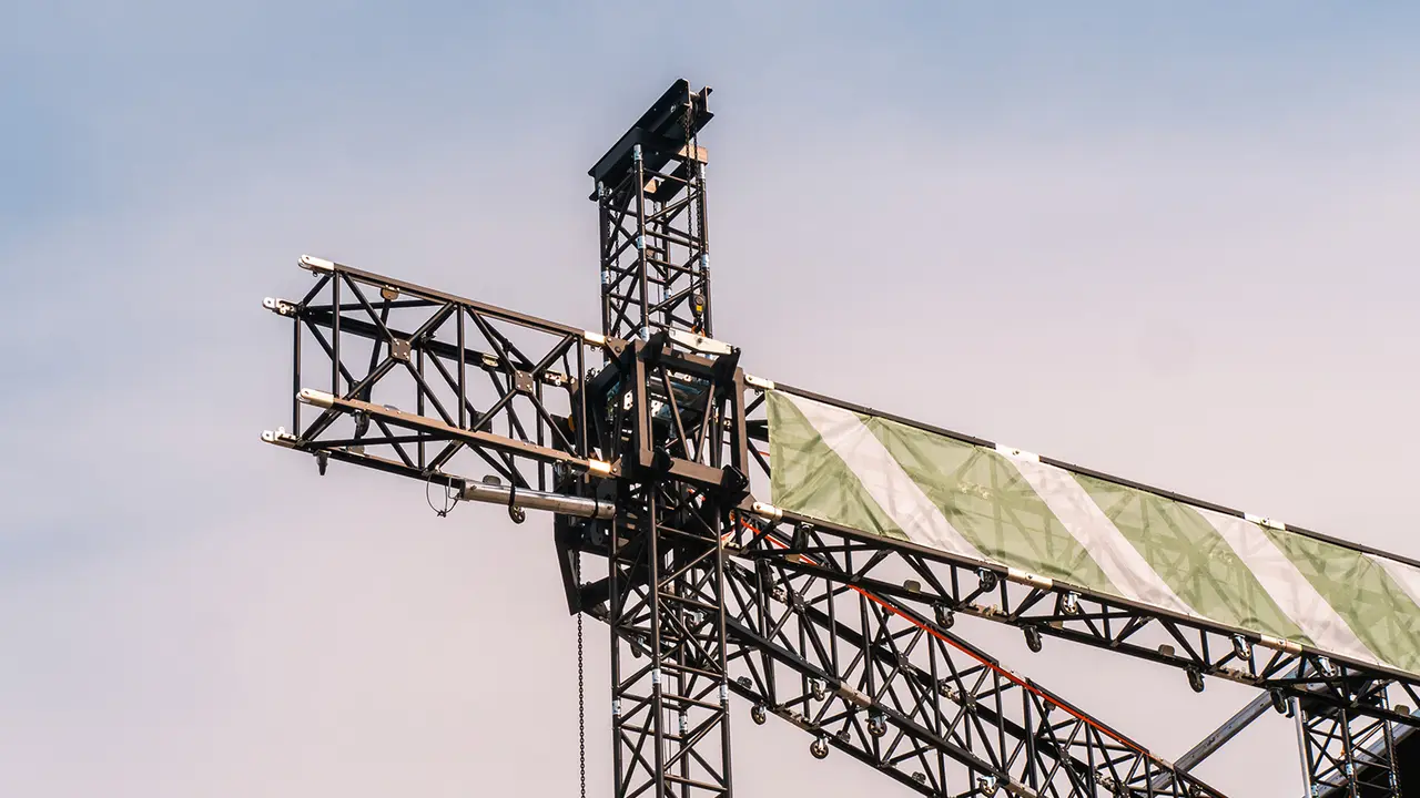 Top of an outdoor ground support truss tower with motor and safety flag against the sky
