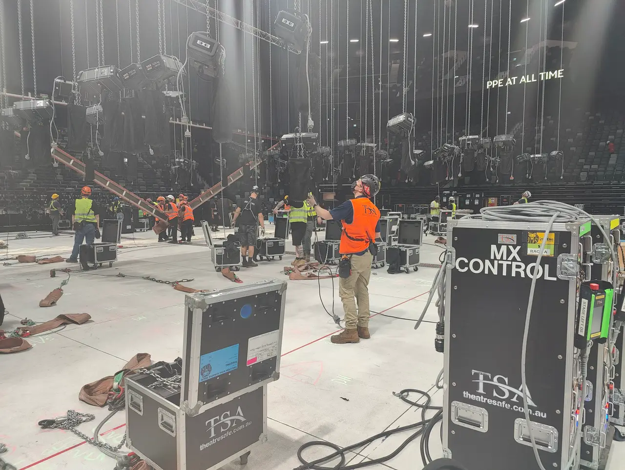 TSA crew rig chain hoists on the arena floor beside MX Control flight cases at Etihad Arena.