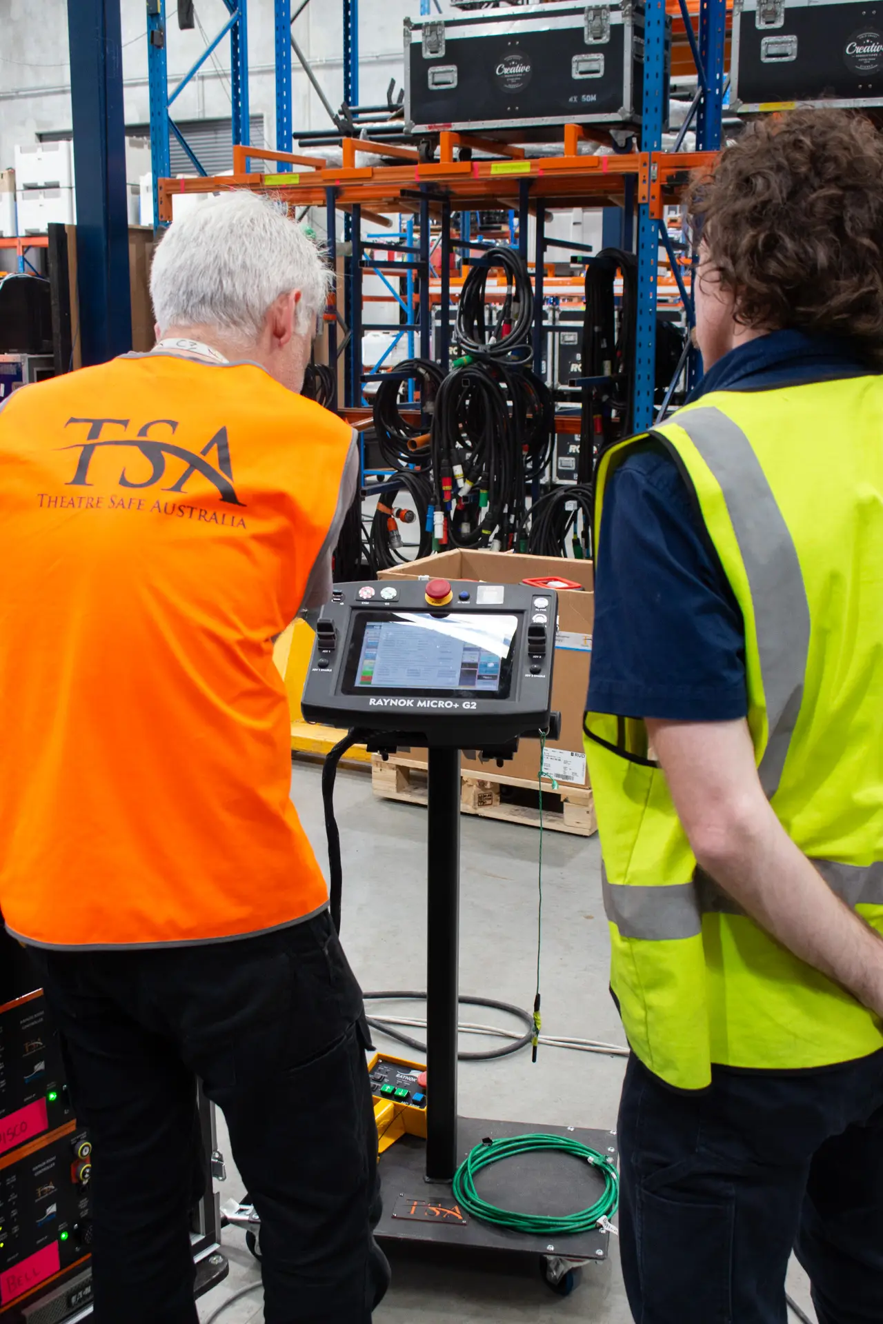 Two TSA staff review a Raynok Micro+ G2 automation controller in the warehouse