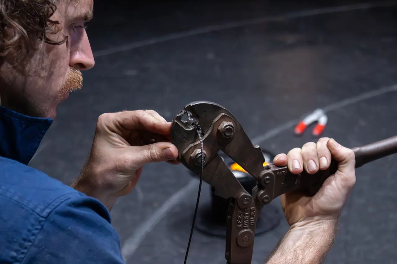 Crew member crimping a wire rope end with a swaging tool on stage.