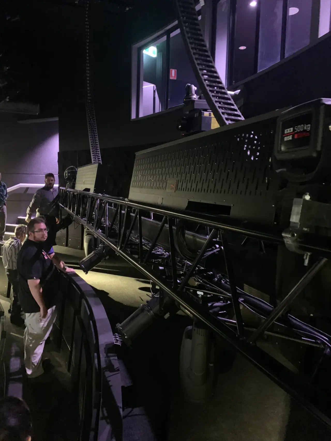 Trainees inspect a chain hoist on a truss track above the auditorium.