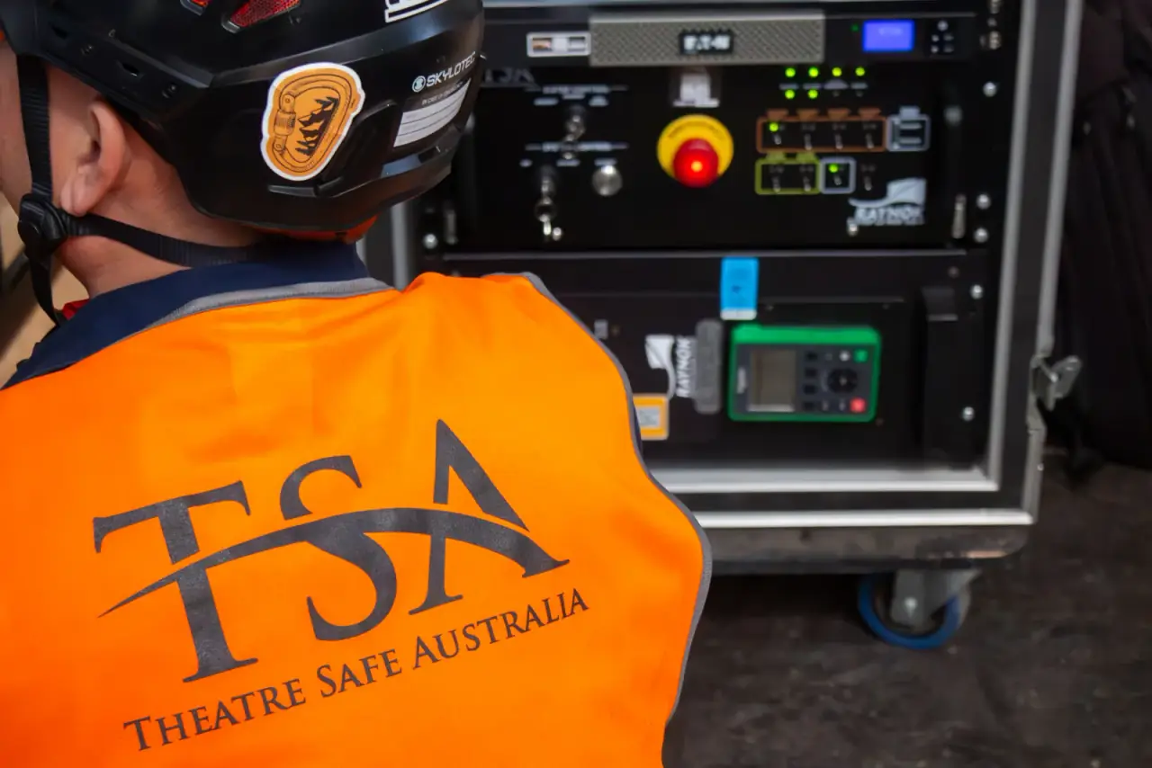 TSA crew member beside a Raynok hoist control rack showing the e-stop and system controls