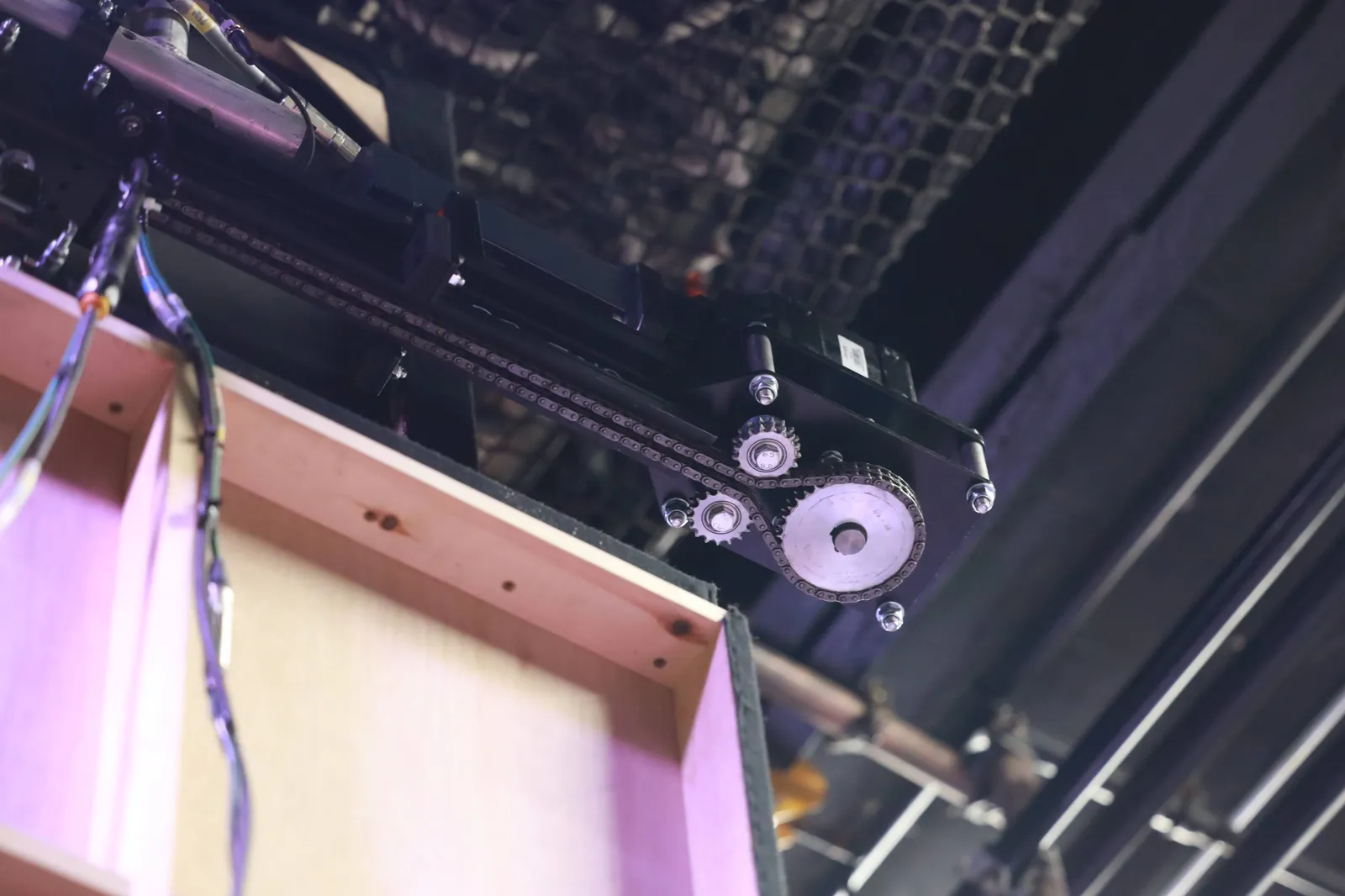Motorised curtain track drive unit with chain and sprockets mounted above a stage set.