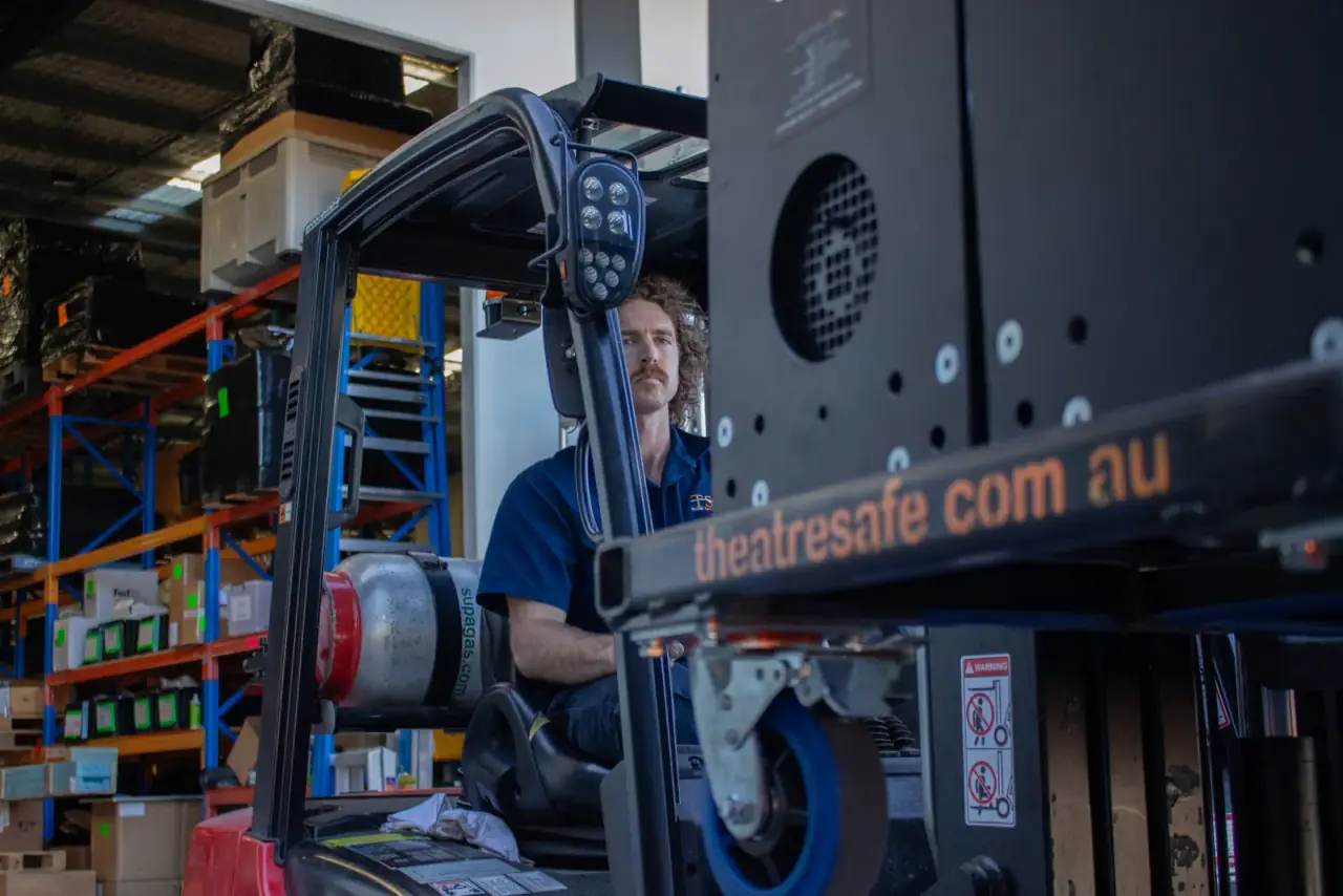 TSA staff member drives a forklift carrying a large winch spool through the warehouse