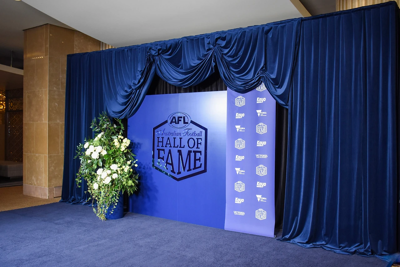 Navy velvet swags over a Hall of Fame backdrop with a white rose arrangement beside it