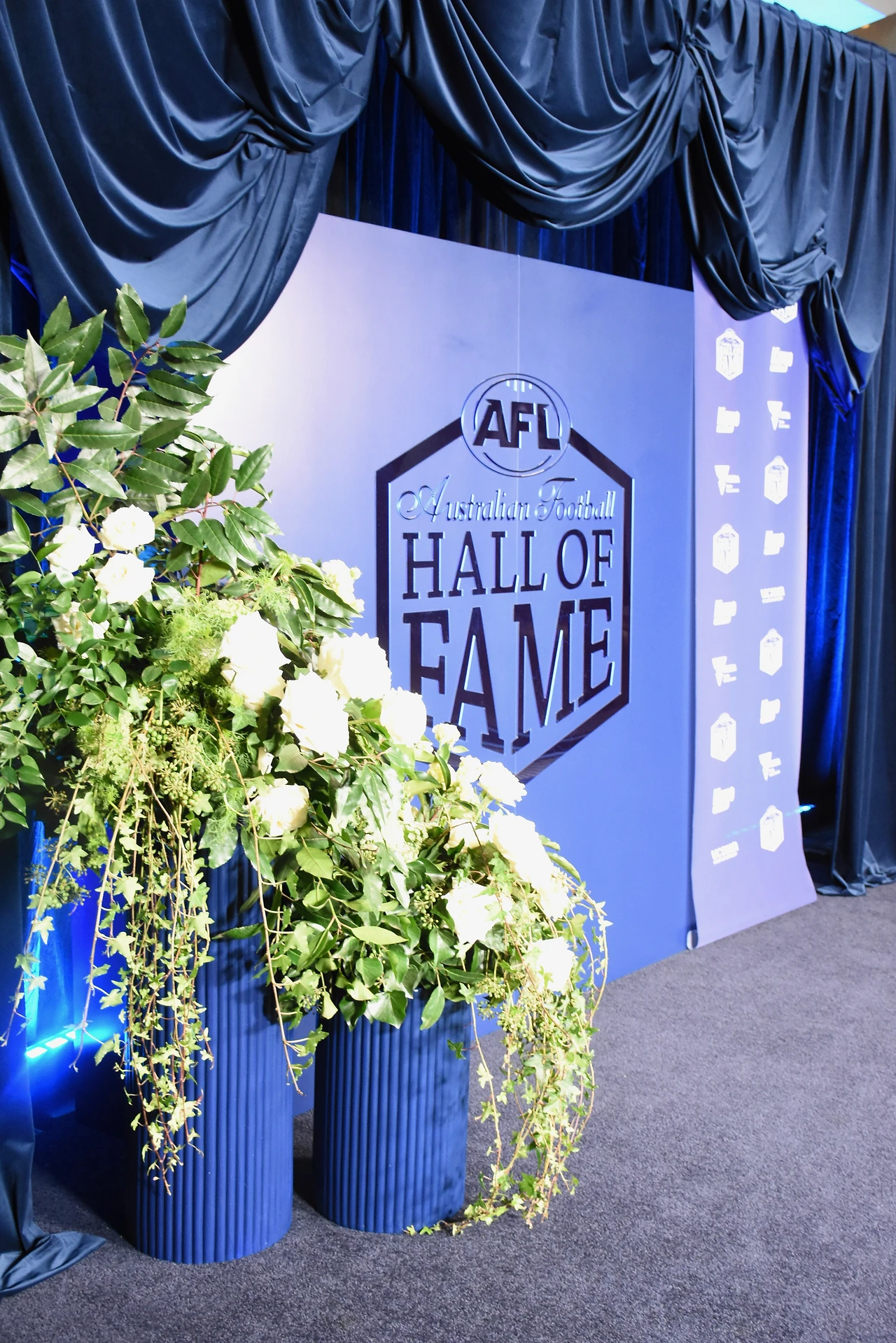White roses and trailing greenery in blue fluted planters against the Hall of Fame backdrop