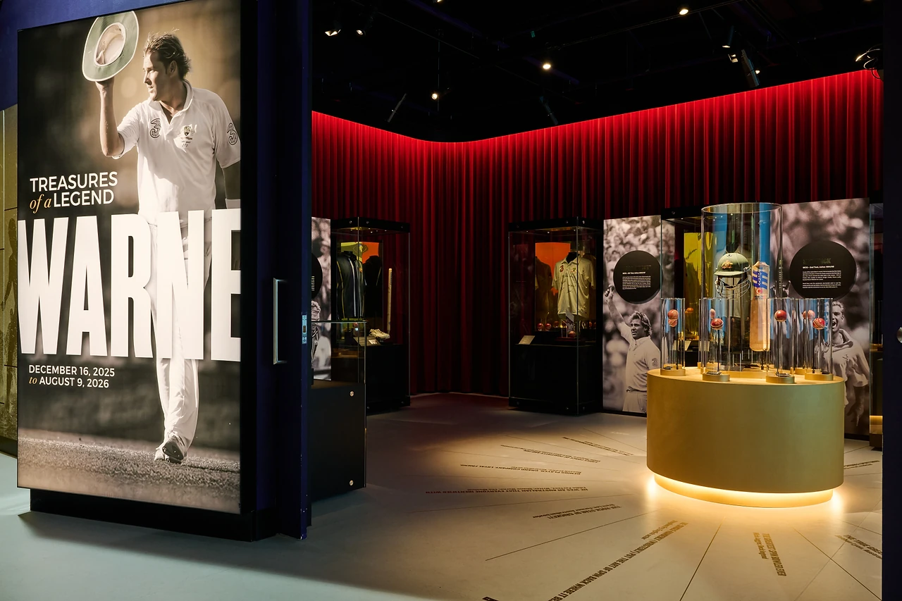 Warne exhibition entry panel beside a lit central plinth and red curtained walls