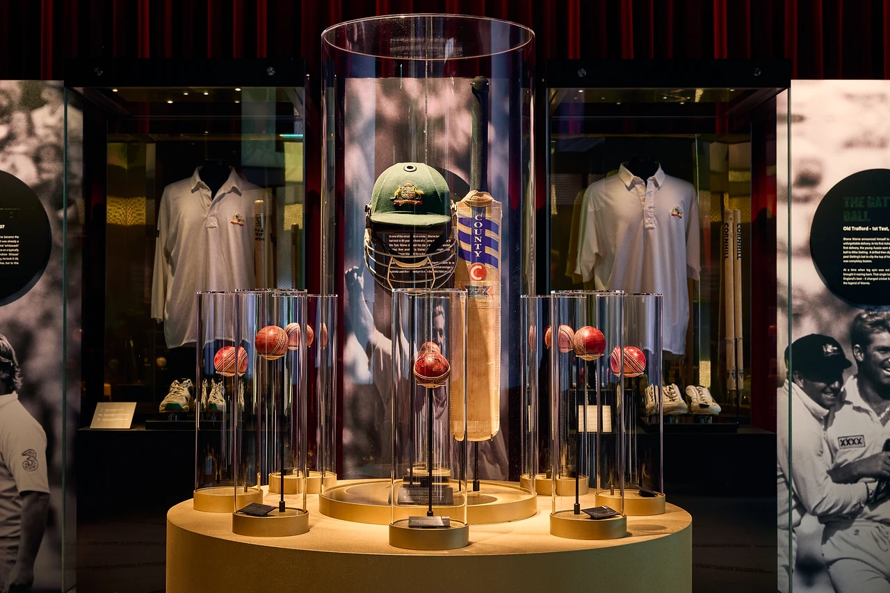 Central glass domes holding a baggy green cap, bat and balls with shirt showcases behind