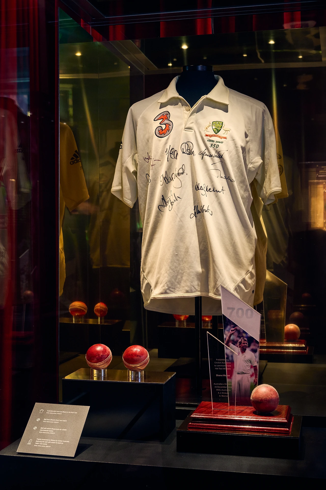 Signed white cricket shirt displayed in a backlit glass showcase with red balls