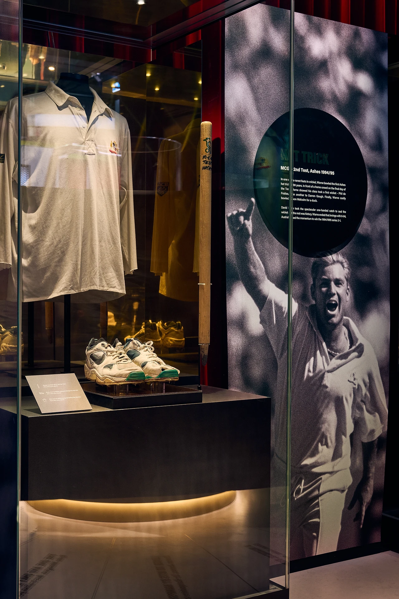 Showcase with cricket shirt and boots beside a large archive photograph