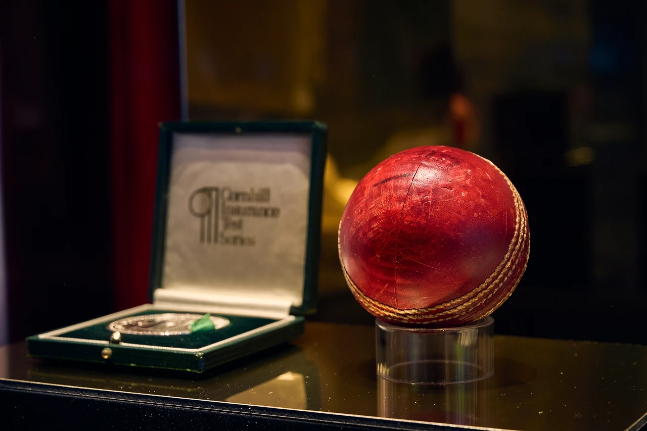 Red cricket ball on a perspex stand beside a presentation case and medal
