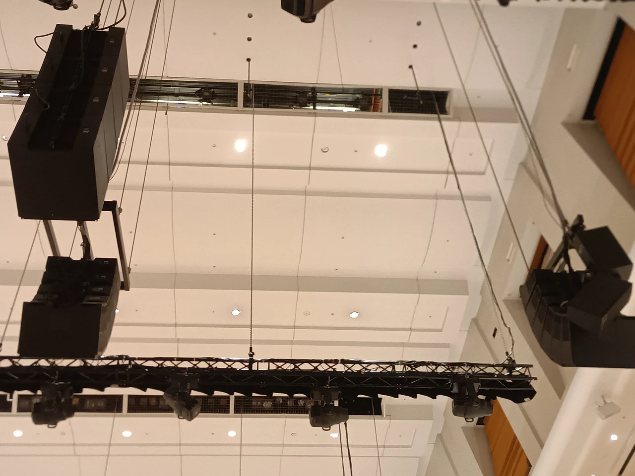 Suspended line-array speakers and lighting truss hanging from ceiling hoists above the hall
