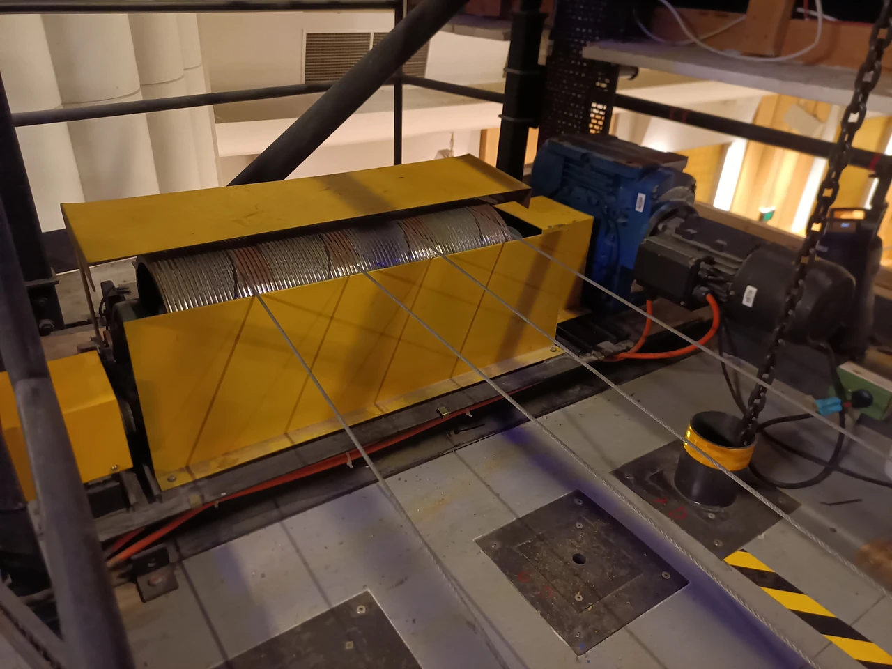 Yellow-guarded winch drum and motor on a technical gallery with a control cabinet beside it