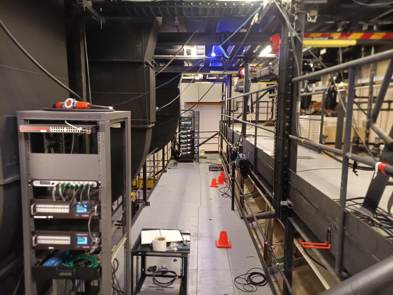 Rack of amplifiers and a hoist on a trolley beam along a black-walled gallery