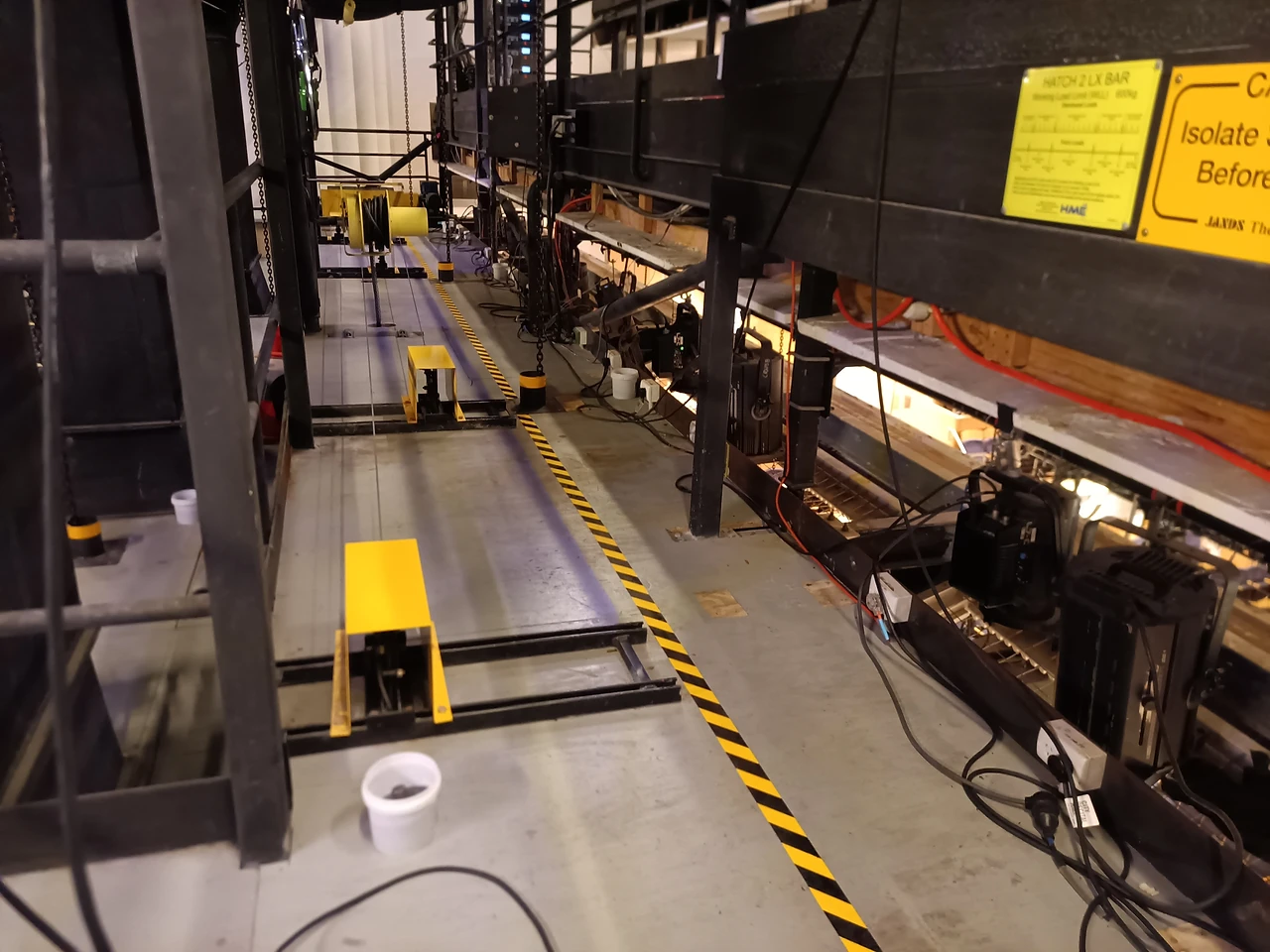 Technical gallery with black and yellow edging, a foot-switch and hoisted equipment along the rail