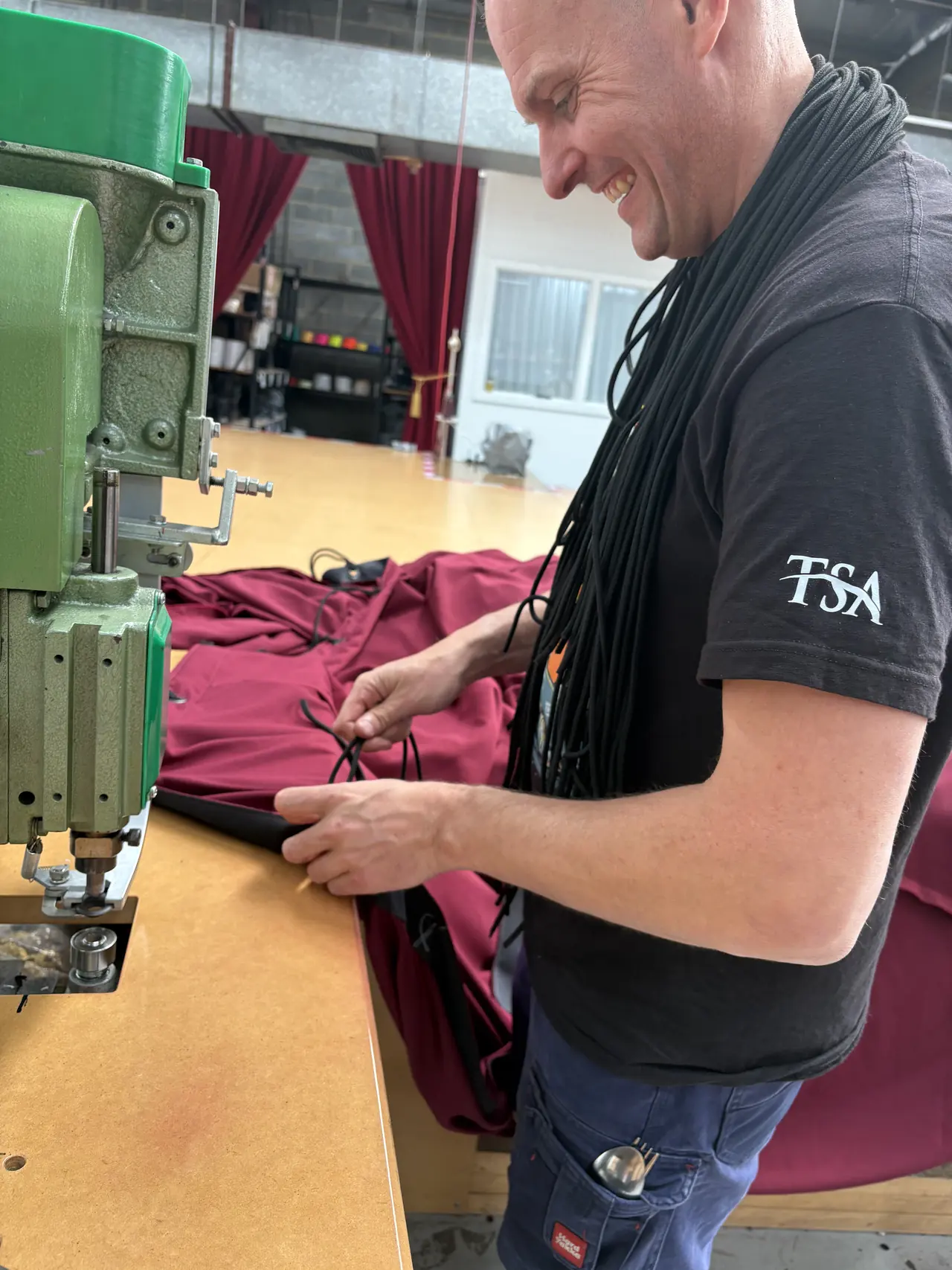 A TSA drape maker fitting black ties to the eyelets of a burgundy roof swag at the eyelet press