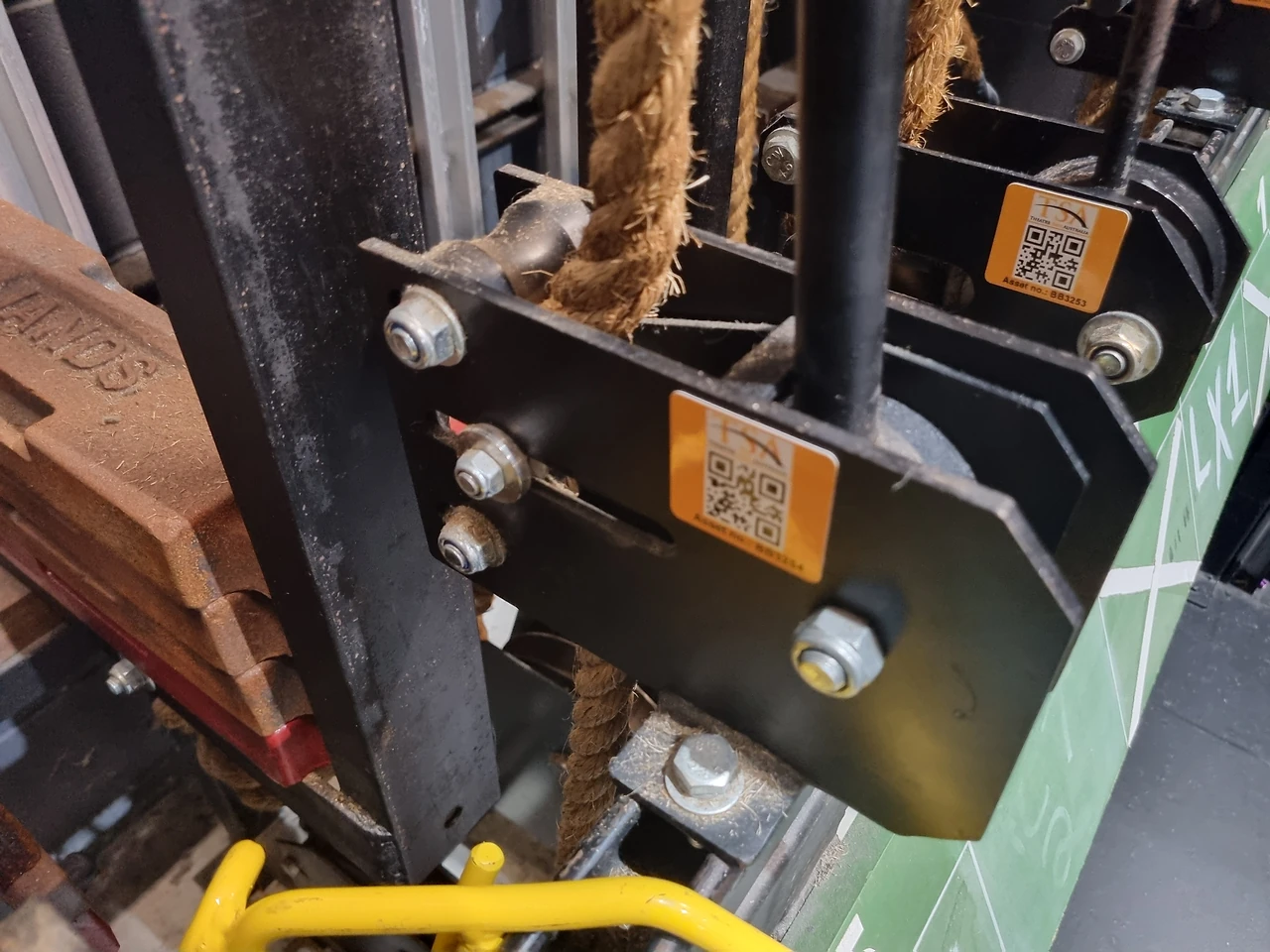 Counterweight carriage bracket with QR asset tag beside manila rope and weights