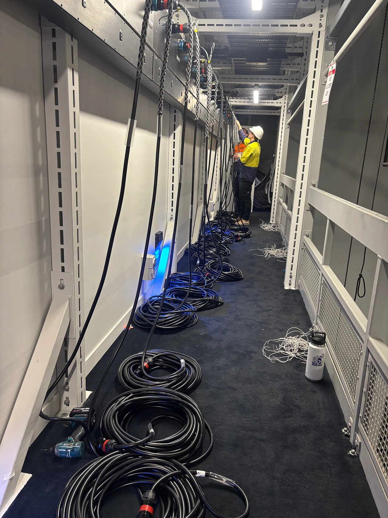 Technician on a side gallery with coiled power leads beneath a row of plug boxes
