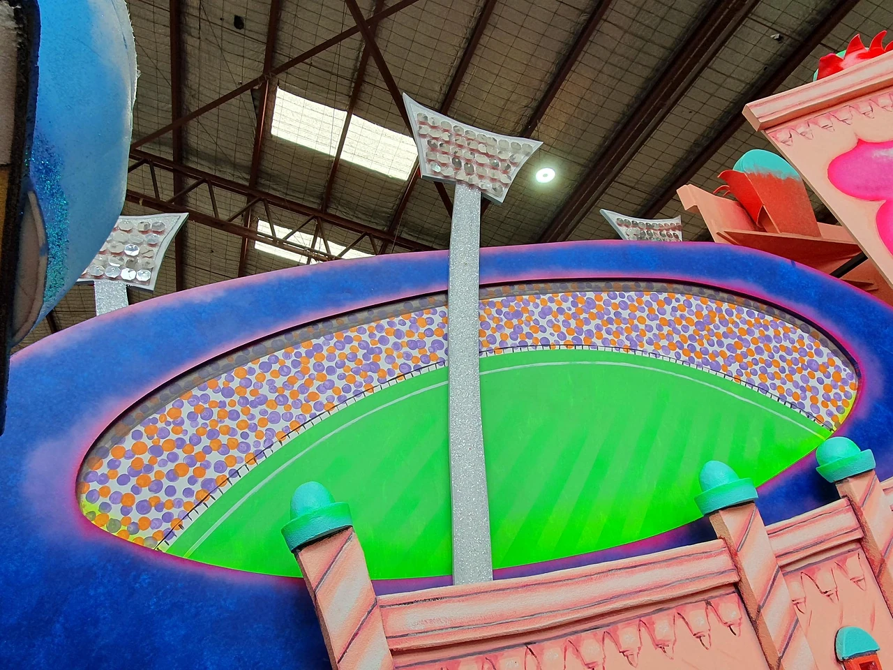 Hand-painted model of a football stadium with floodlights and crowd on a float