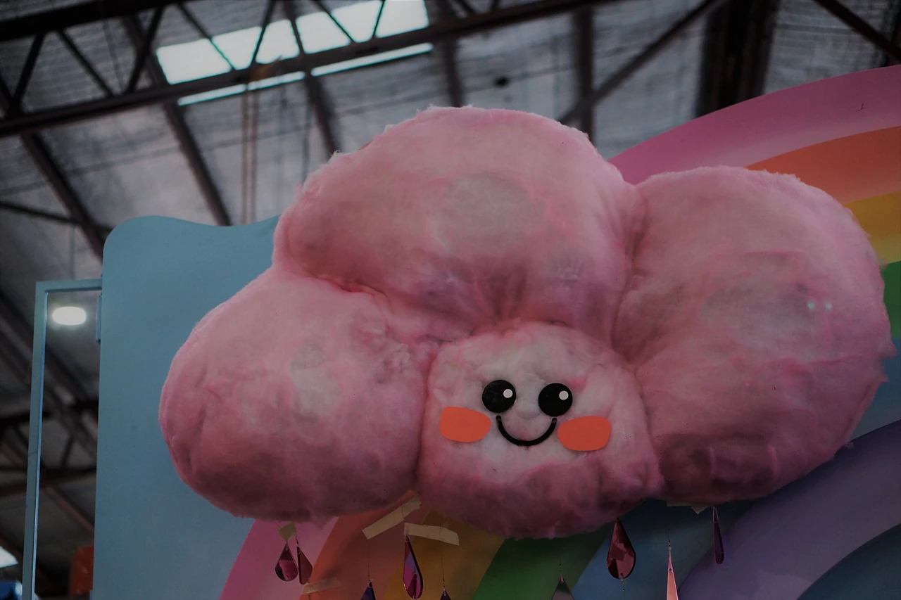 Pink cotton-candy cloud with a smiling face in front of a rainbow