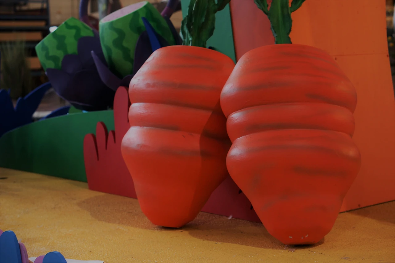 Two oversized foam carrots on a float deck beside green foliage
