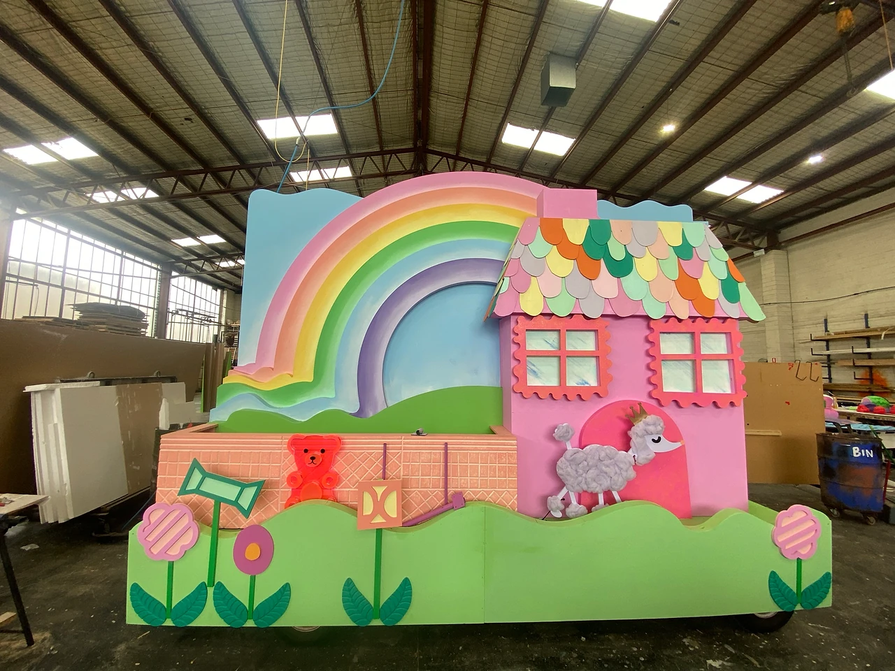 Pastel parade float with rainbow backdrop and pink shingle-roofed cottage in the workshop