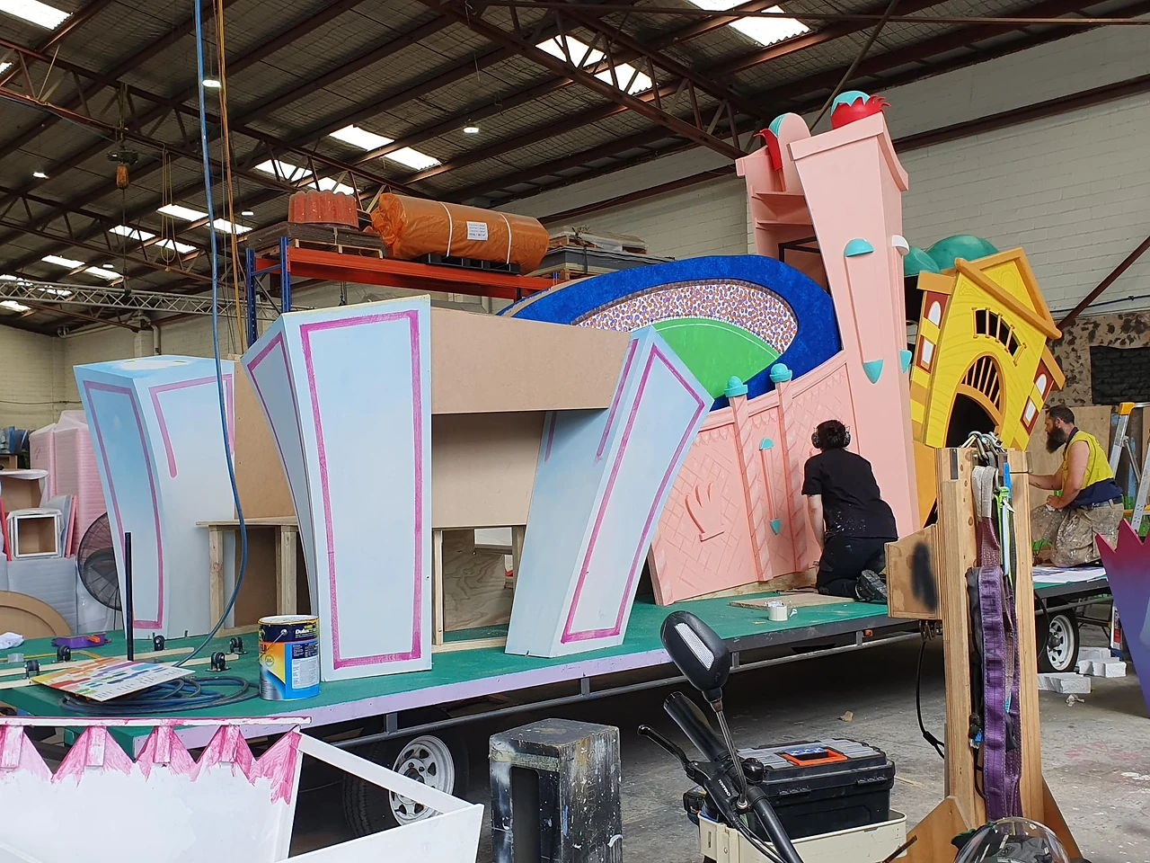 Float in build with stadium and clock tower scenery, crew at work in the workshop