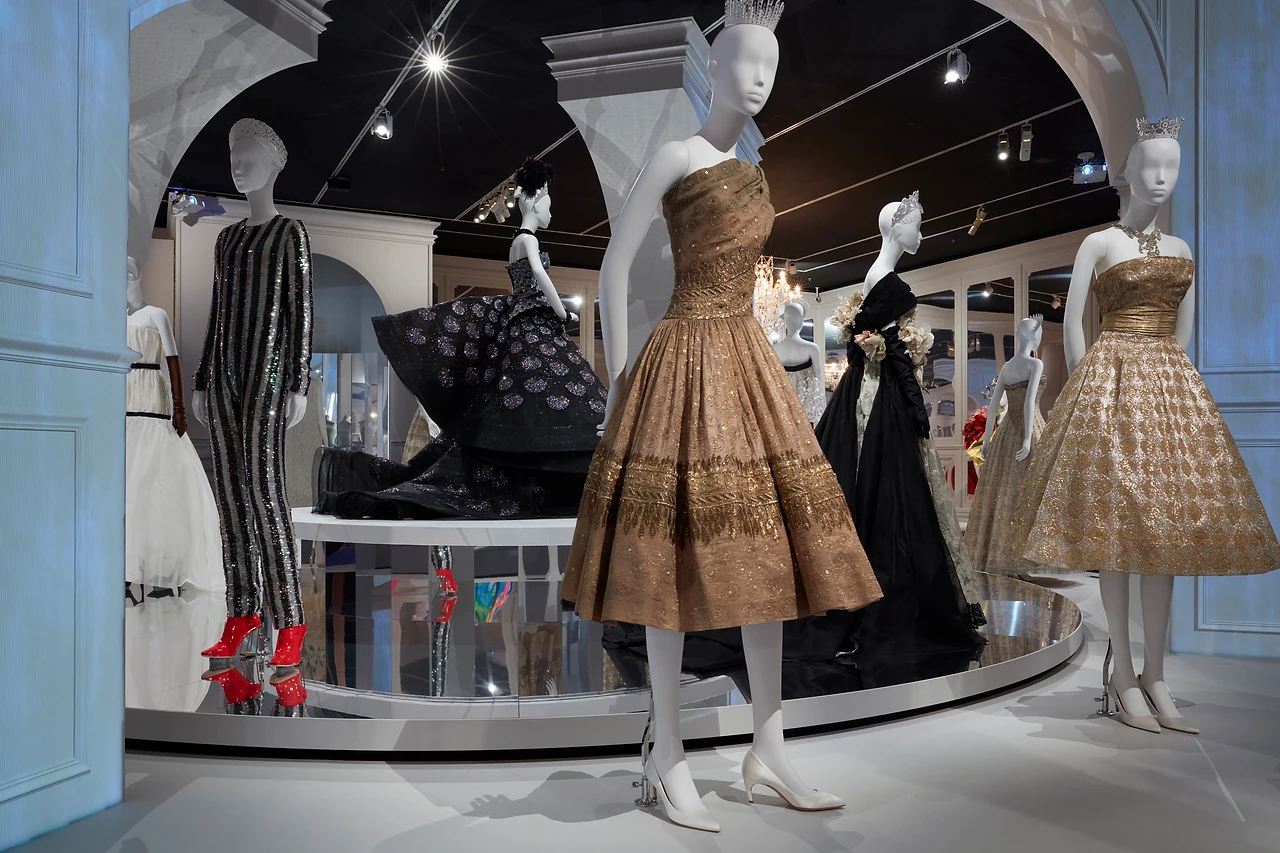 Two Dior cocktail dresses in the foreground of a gallery with blue arches and a round mirrored stage