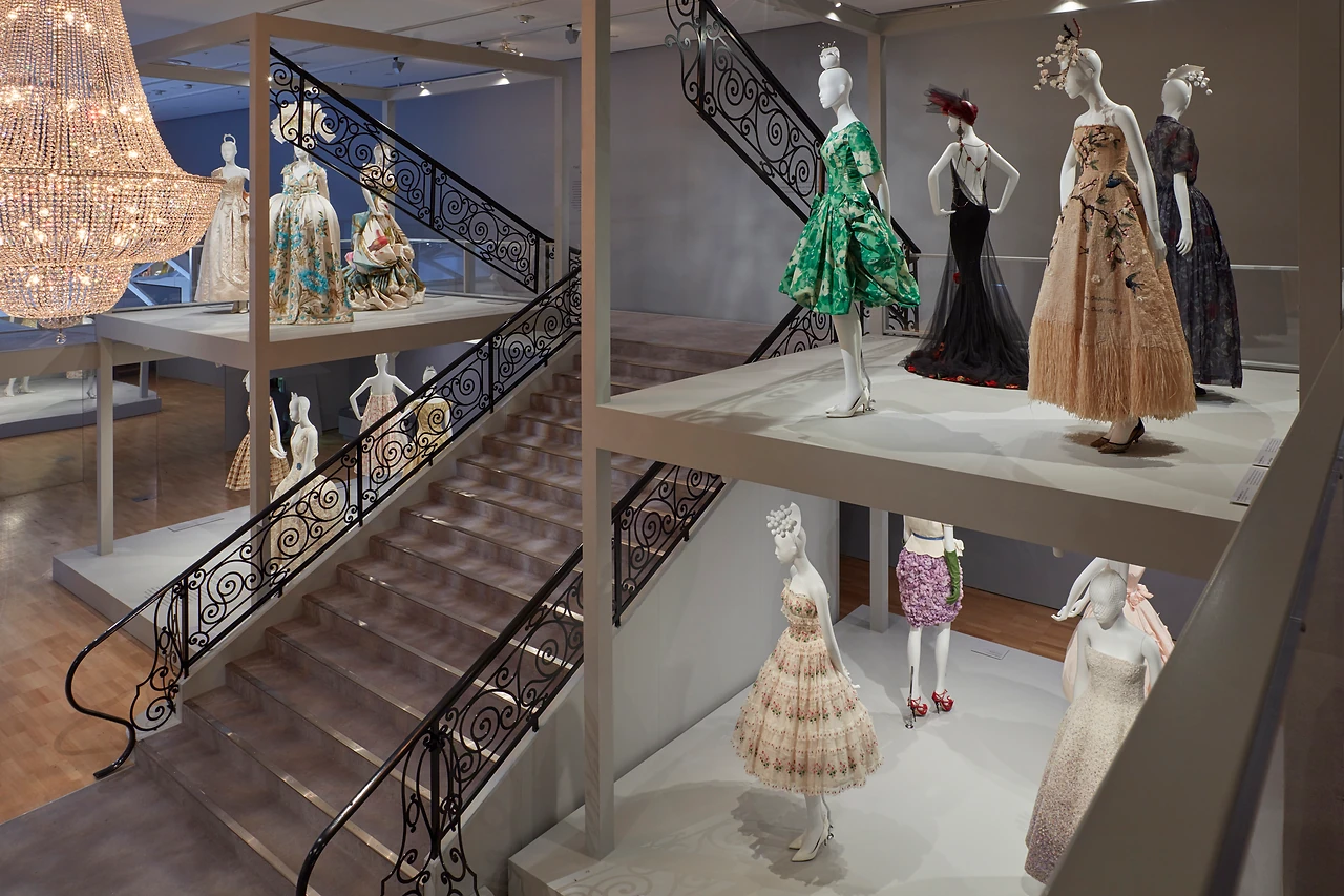 Gallery staircase with wrought iron balustrade and gowns displayed on timber landings