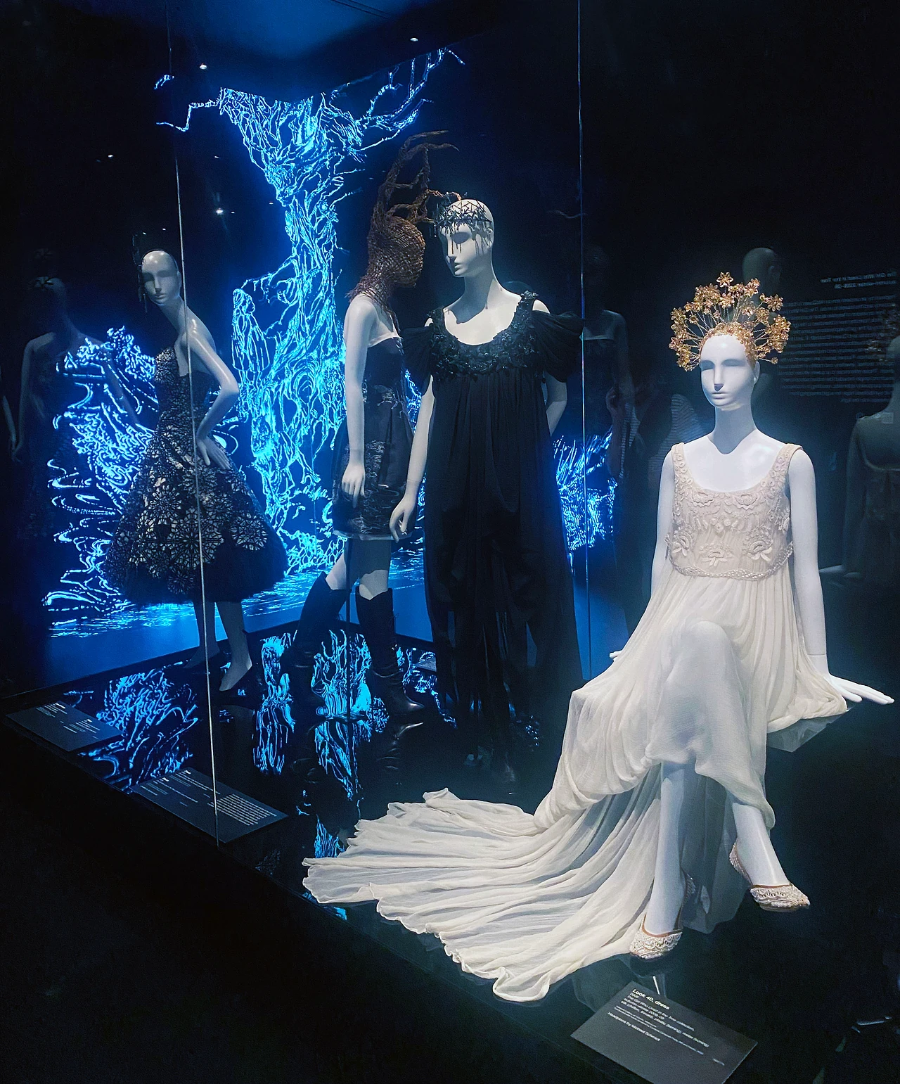Mannequins in dark and white gowns on a black stage against glowing blue branching graphics