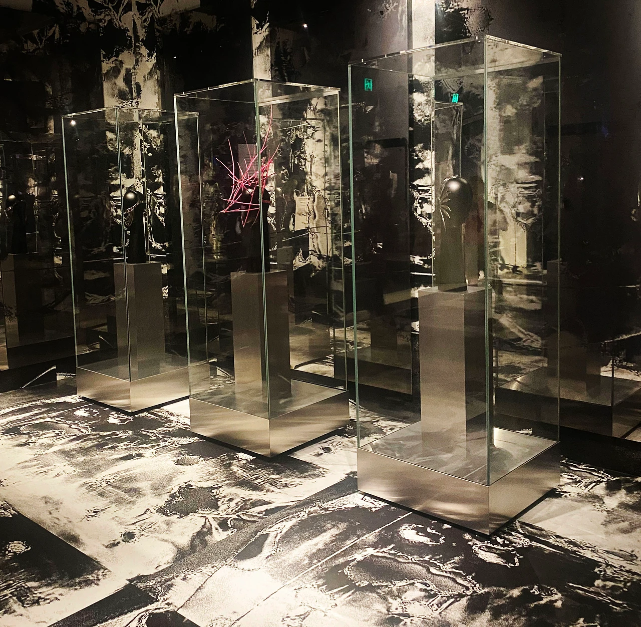 Glass showcases on mirror plinths over a black and white printed floor