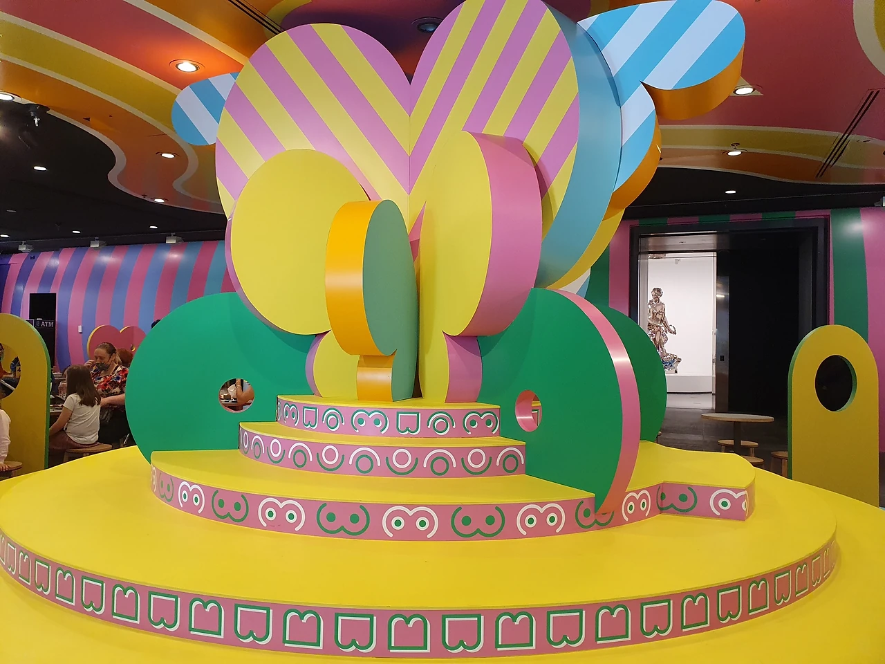 Tiered yellow circular stage with oversized heart and butterfly shapes in a bright children's gallery