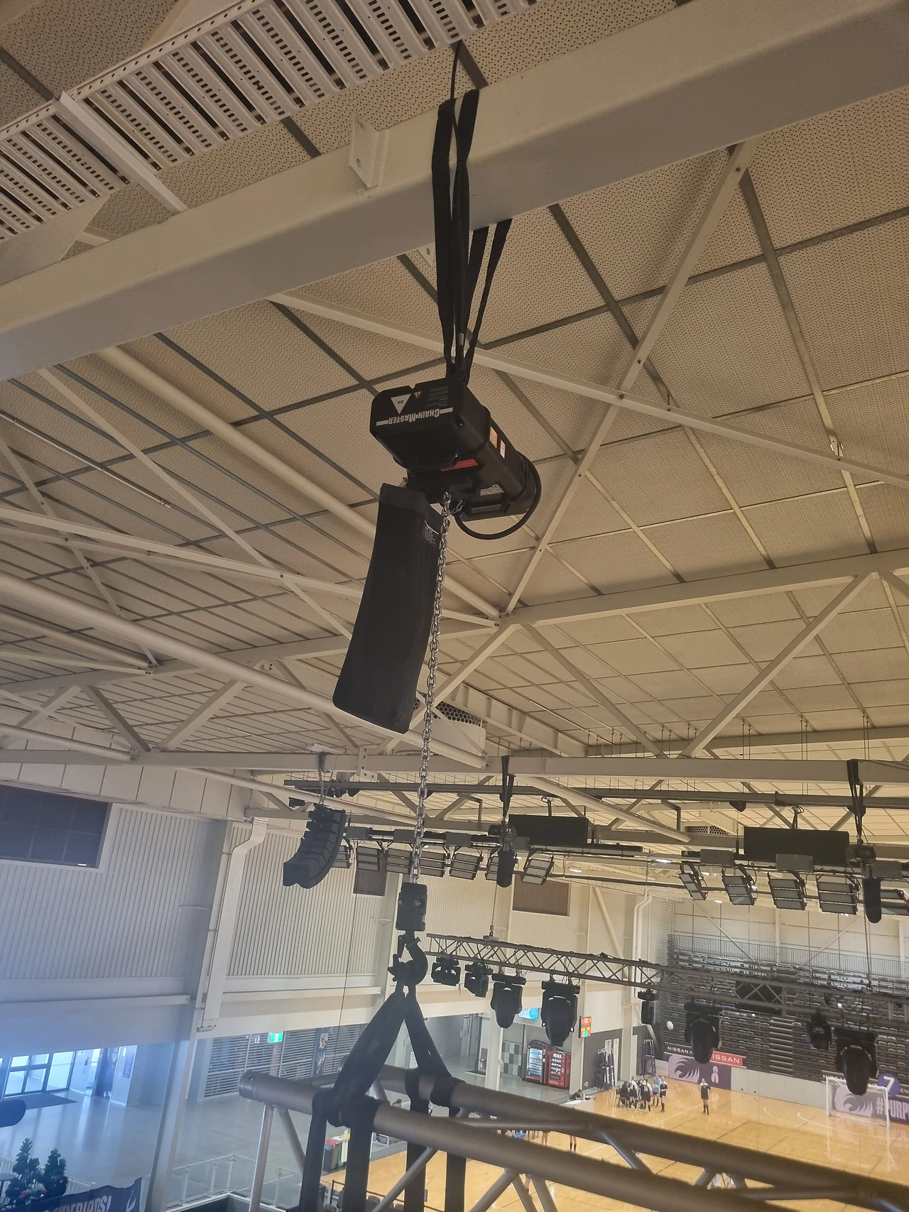 Hoist and cable hanging from roof steel with lighting trusses behind