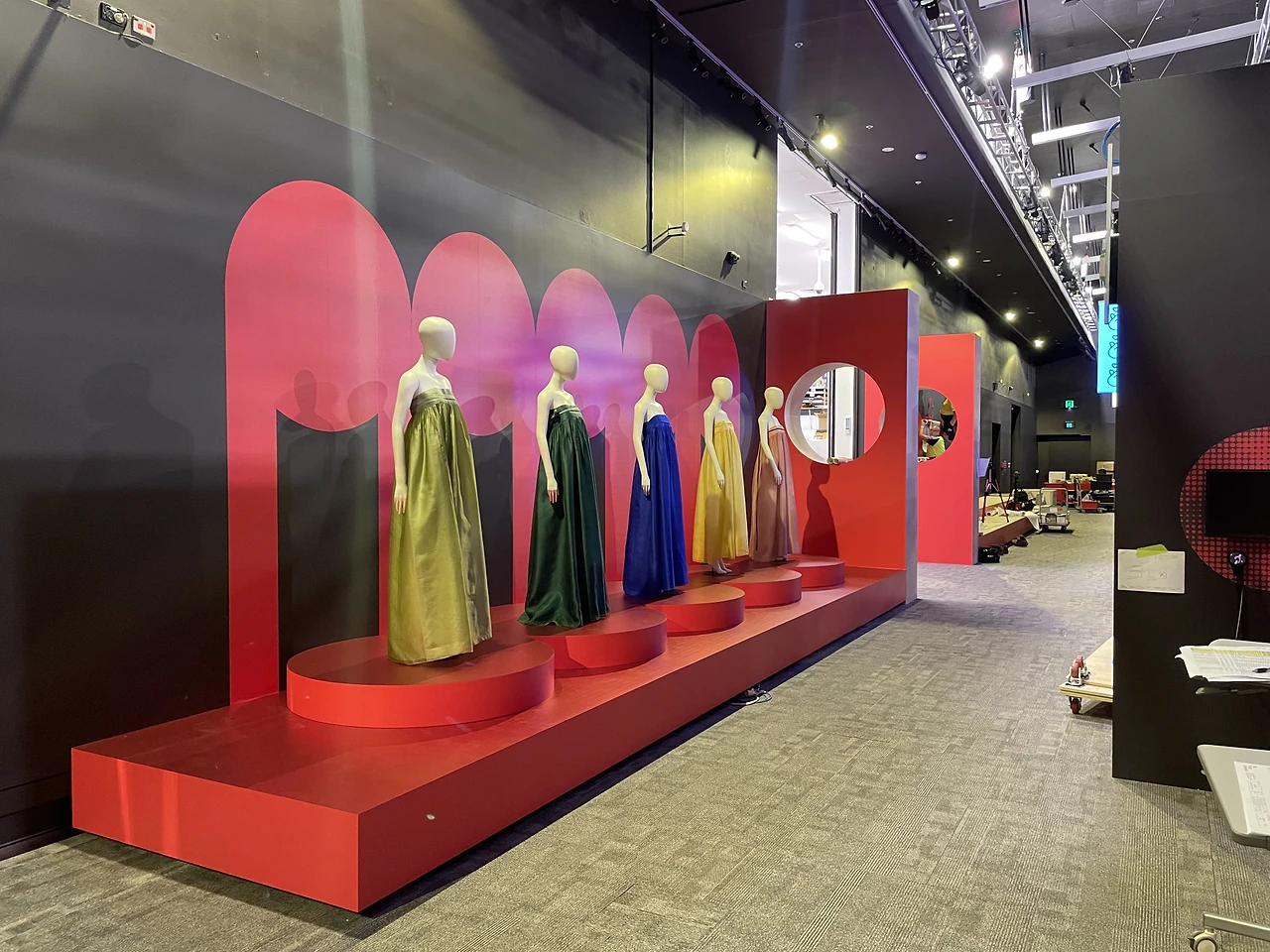 Long red plinth with five gowns in front of scalloped red arch walls